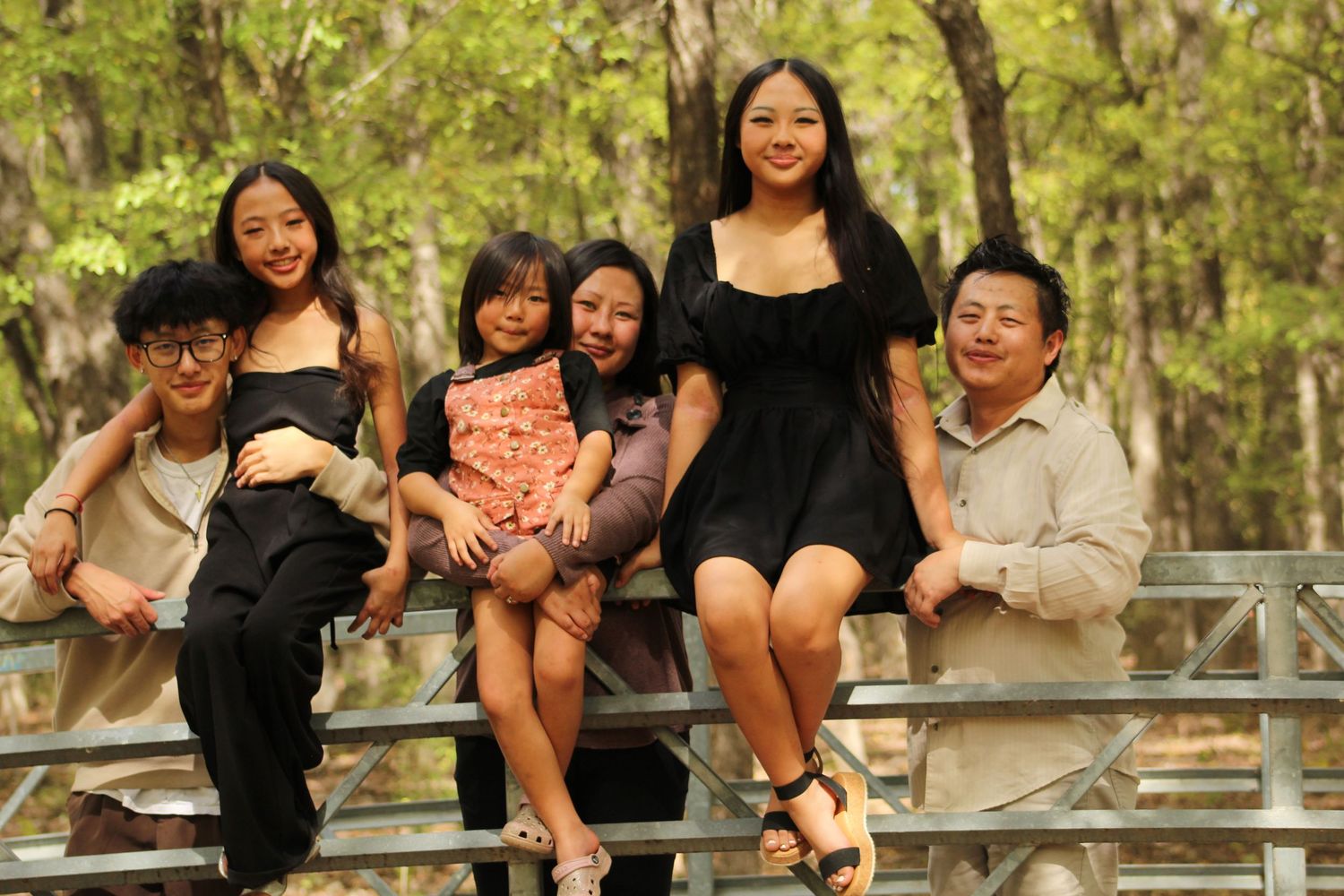 A joyful family photo session captured outdoors on a wooden railing in a natural setting.