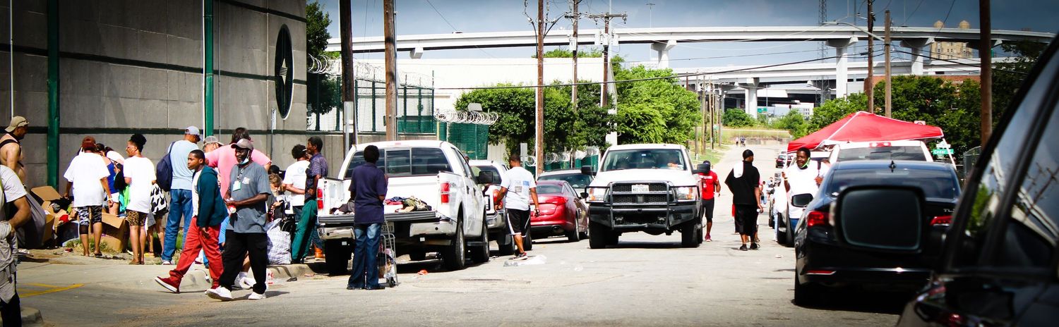 Long panoramic view of people and vehicles outside a commercial building.
