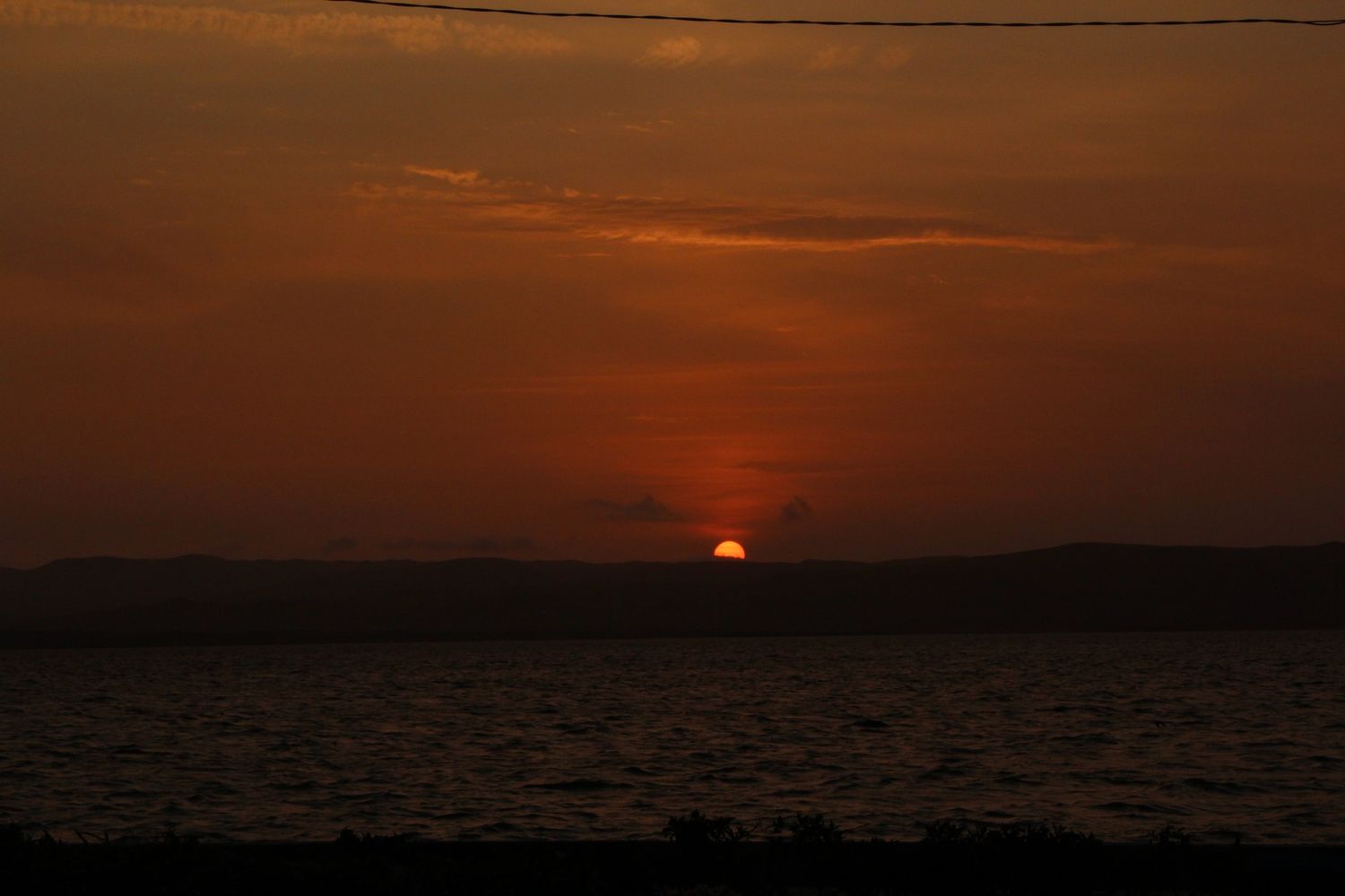 Dramatic orange and red sunset over calm ocean waters with dark silhouetted horizon.