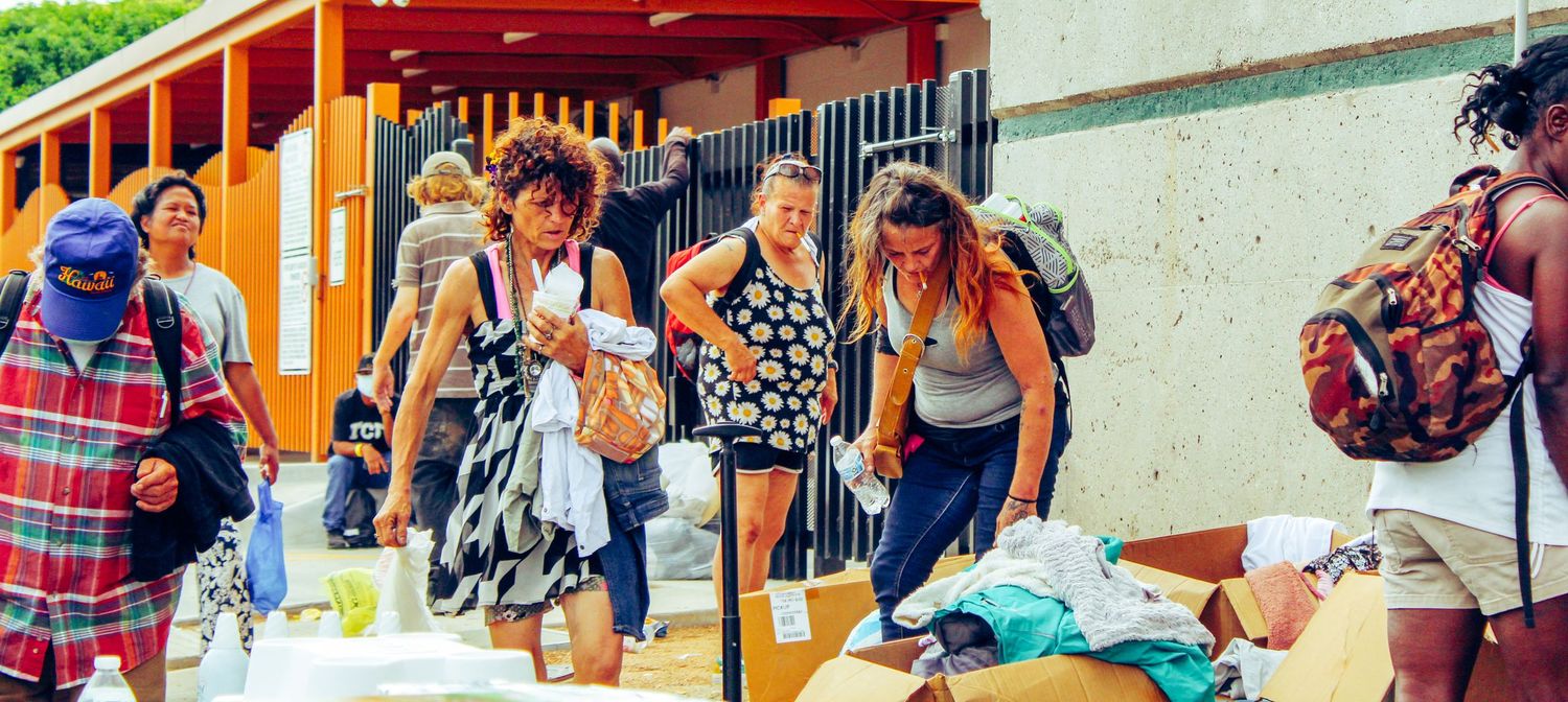 Group of people gathering outside a building entrance near tables with supplies.