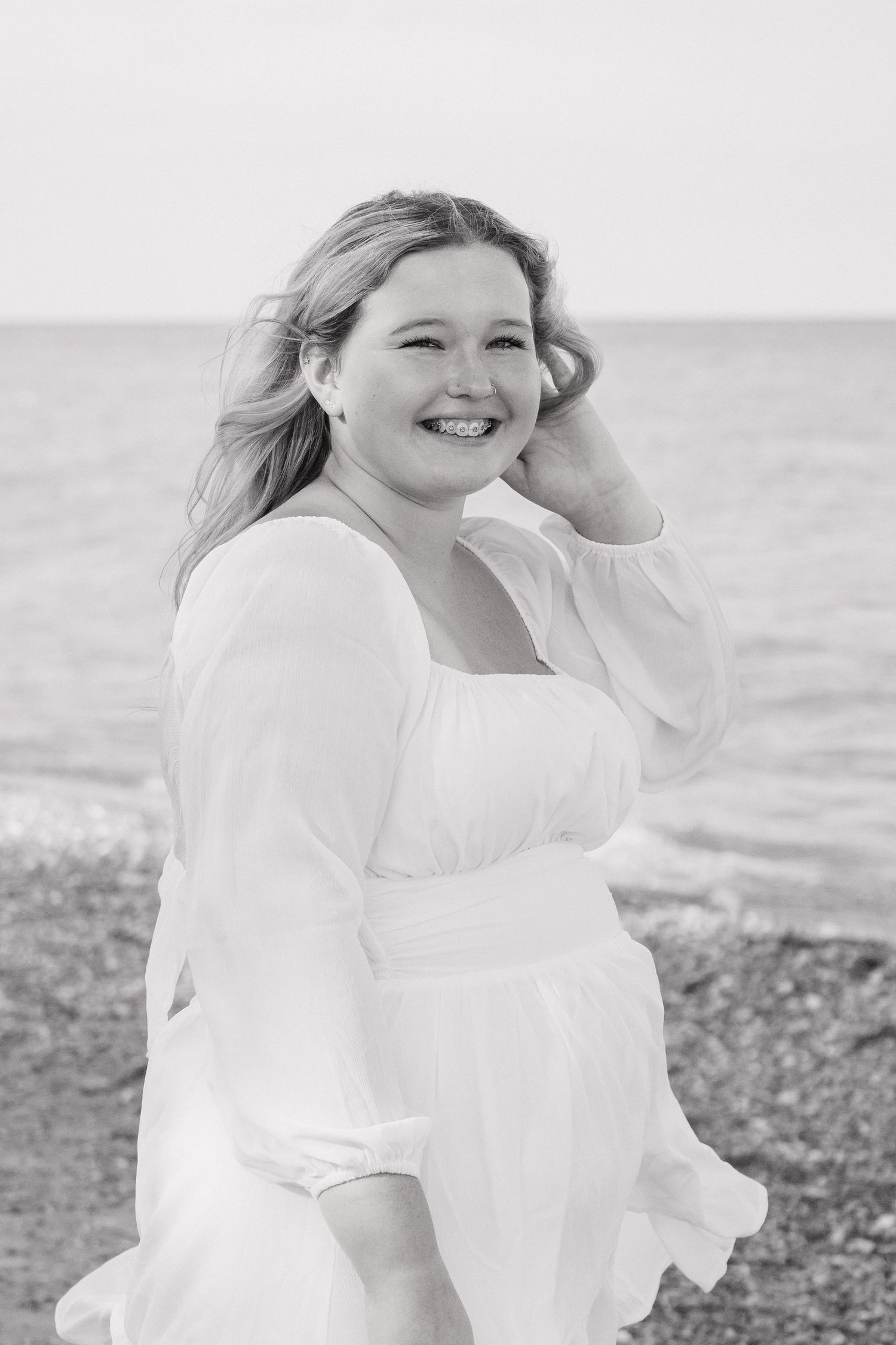 Black and white portrait of smiling blonde woman in white dress at beach.