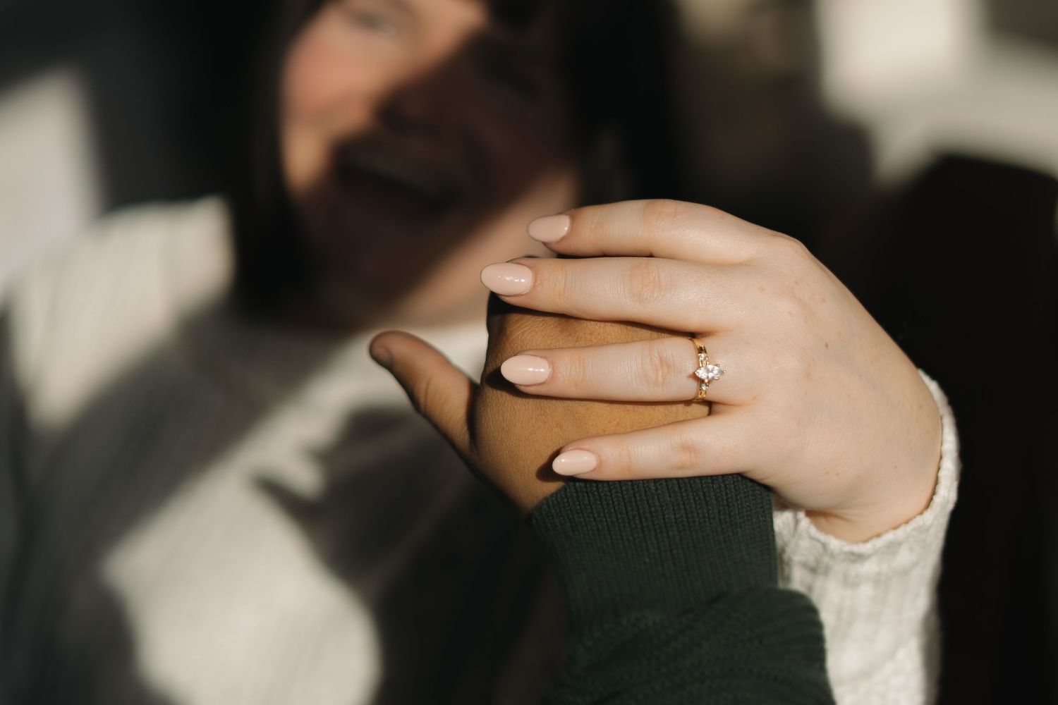 Close-up of a woman's hand displaying a diamond engagement ring while holding a brown coffee mug.