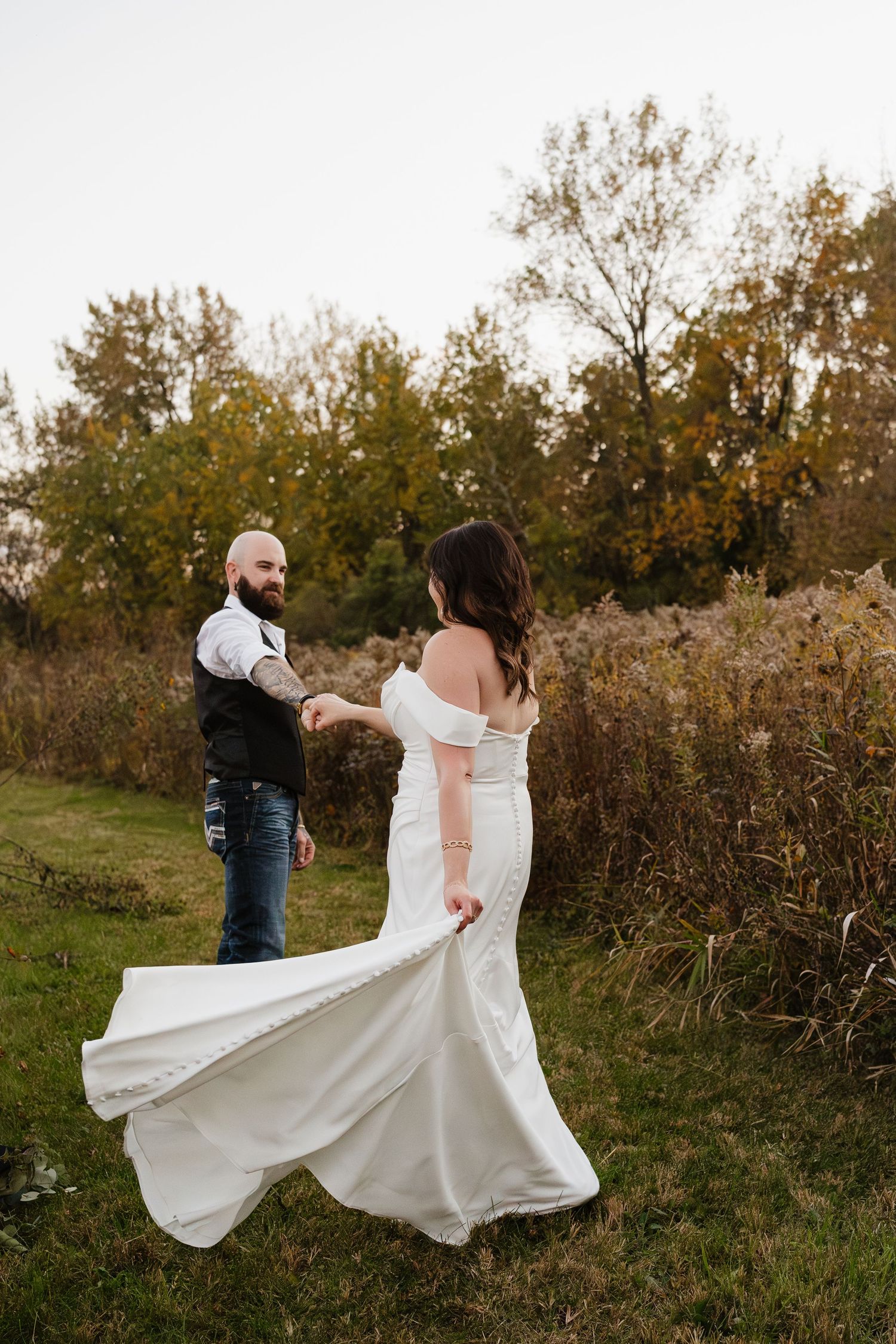 Groom holds bride's hand as she twirls her white wedding gown in a scenic fall outdoor setting.