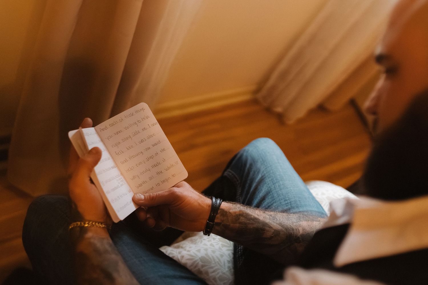 Tattooed groom reading handwritten vows while seated before his wedding ceremony.
