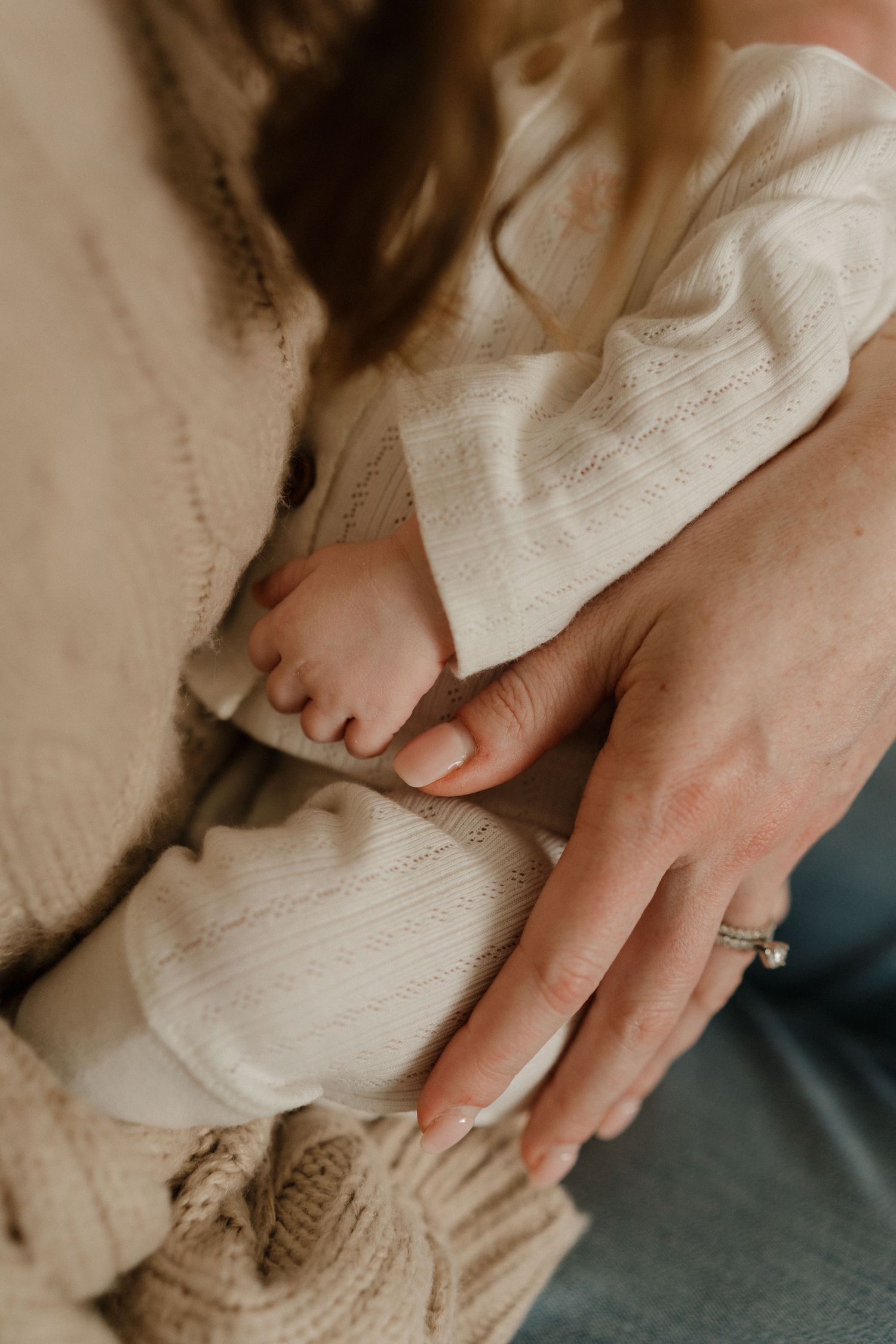 Close-up of a mother cradling her newborn baby's tiny feet in her hands, wearing a cozy knit cardigan.