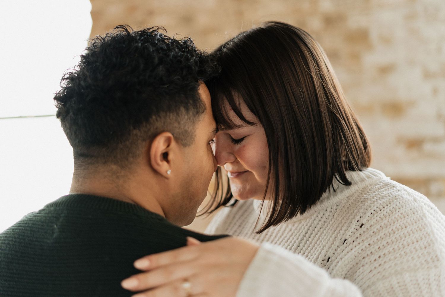 Romantic interracial couple sharing an intimate moment, touching foreheads tenderly while embracing indoors.