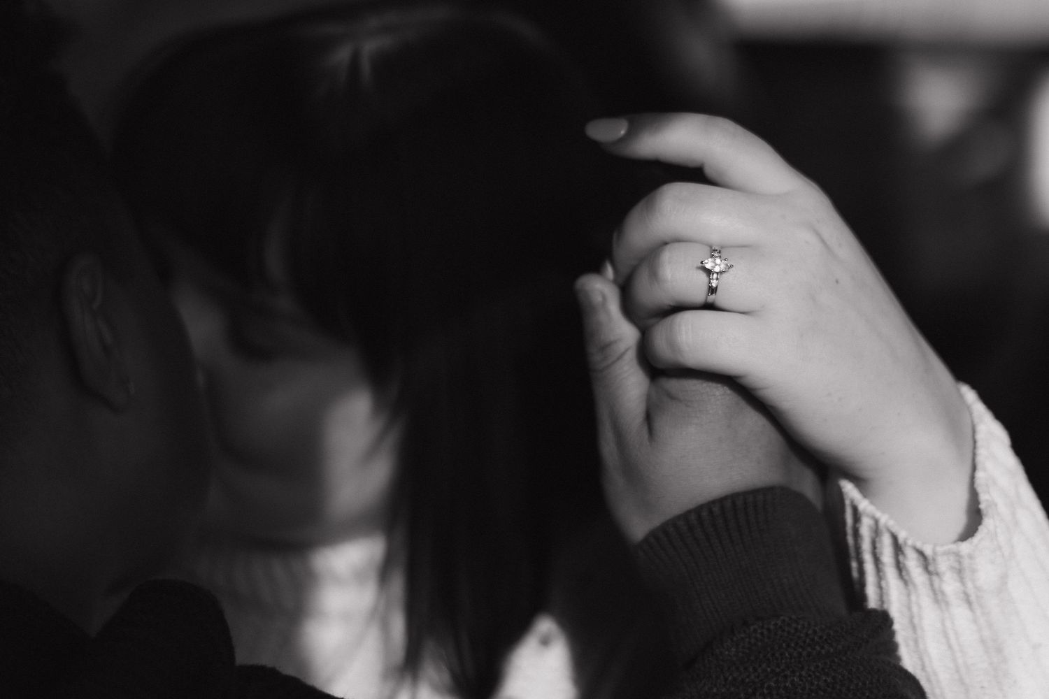 Black and white photo of a woman with an engagement ring on her hand resting on her head.