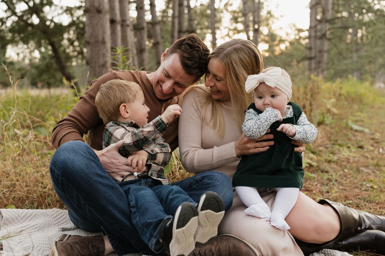 Happy young family of four sitting together outdoors in pine forest during fall season.