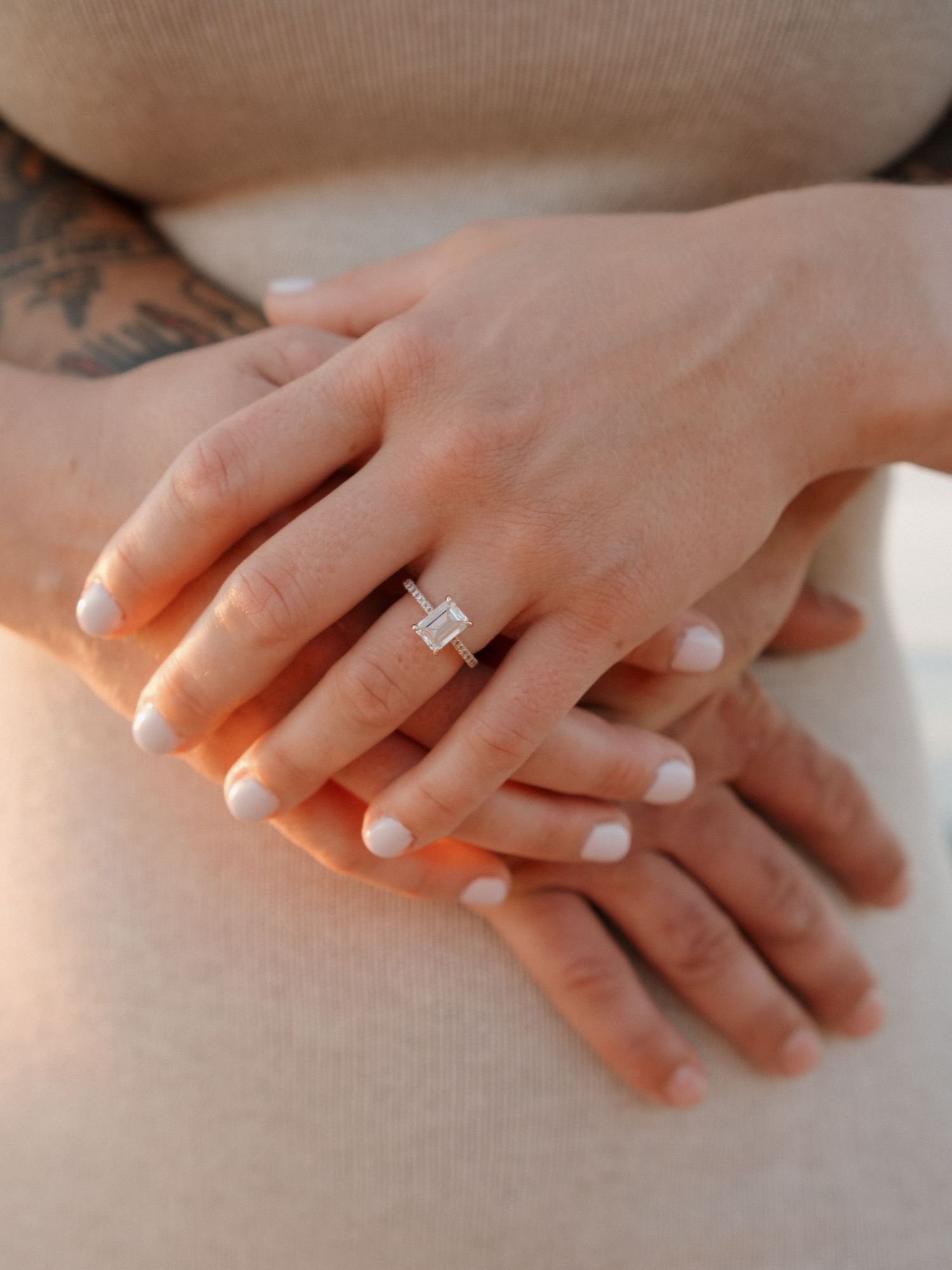 Close-up of hands with white manicure wearing an emerald cut diamond engagement ring on ring finger.