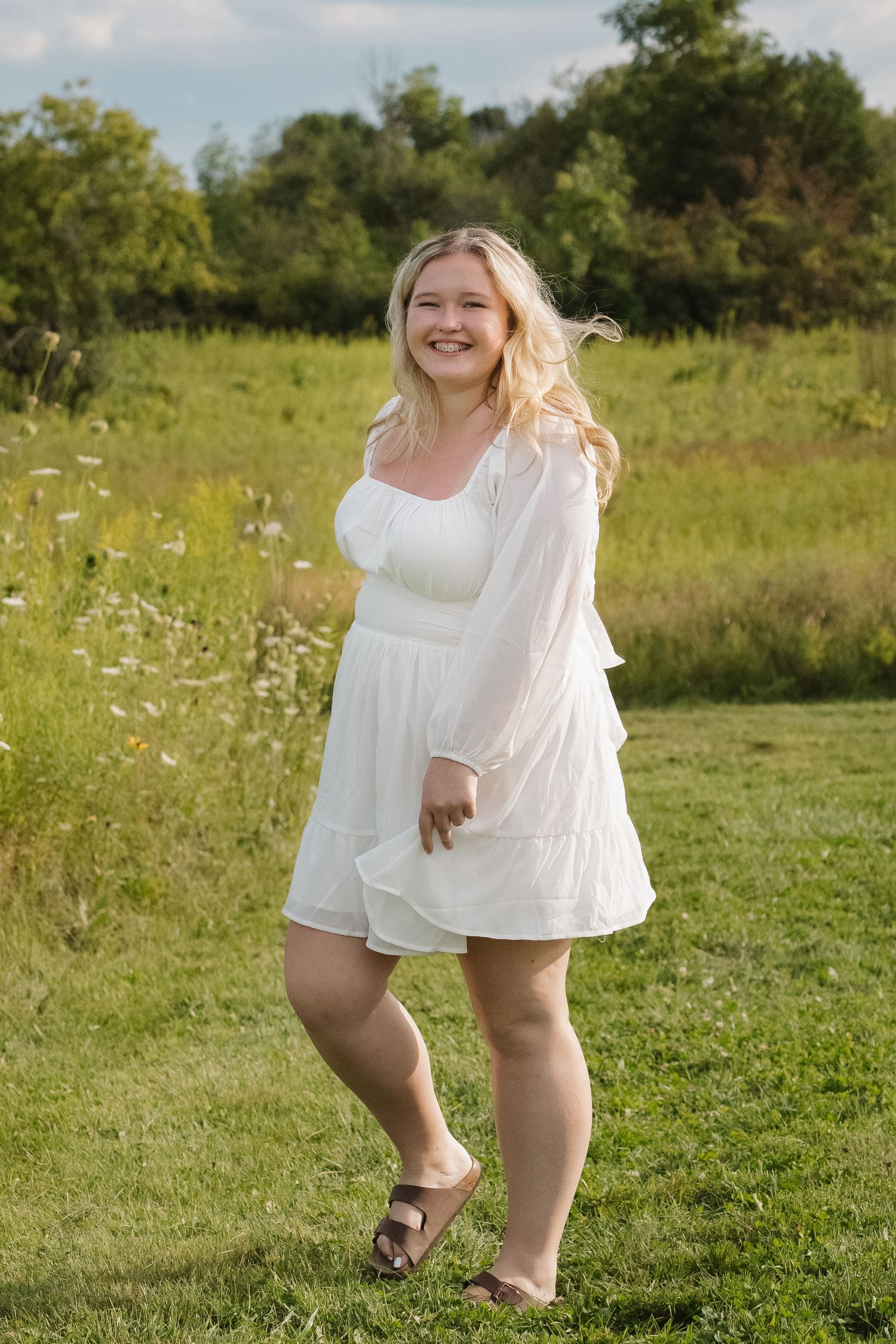 Happy blonde teen in white dress laughing outdoors in grassy field.