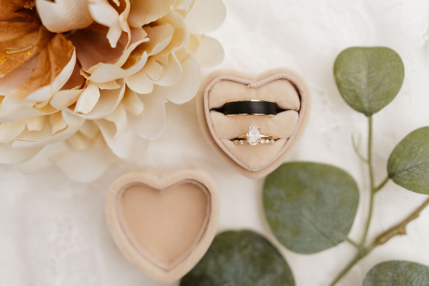 Diamond engagement ring and black wedding band in heart-shaped velvet box with flowers and eucalyptus.