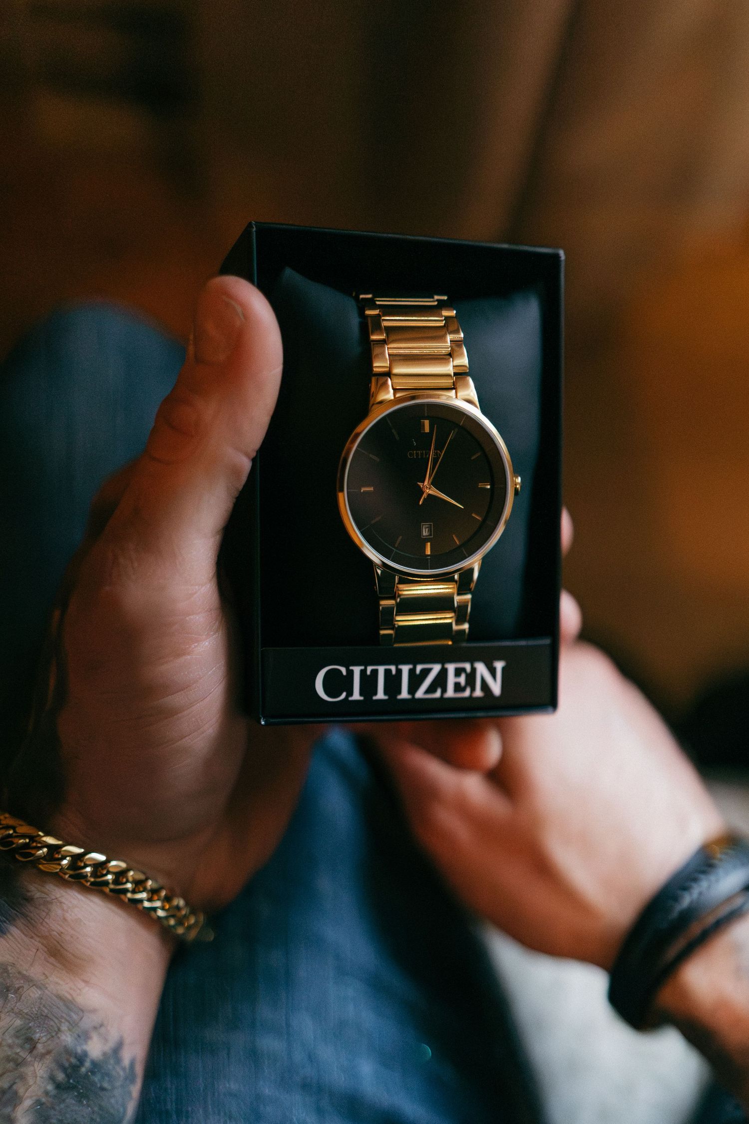 Hands holding a Citizen gold-tone watch with black dial in its box.