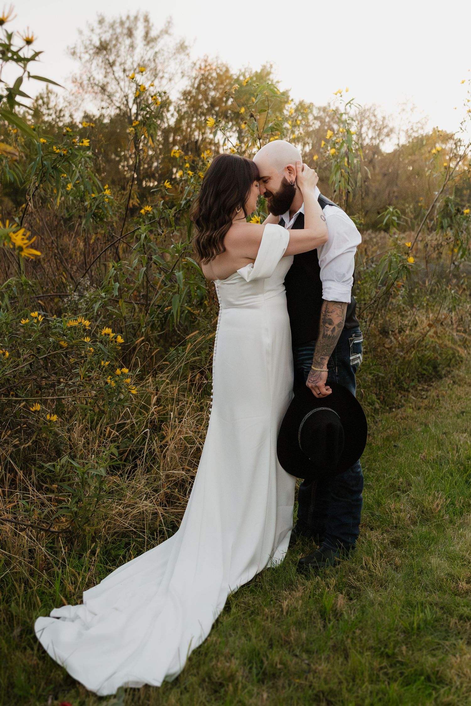 Bride and groom sharing a romantic kiss in a golden sunlit field surrounded by wildflowers.