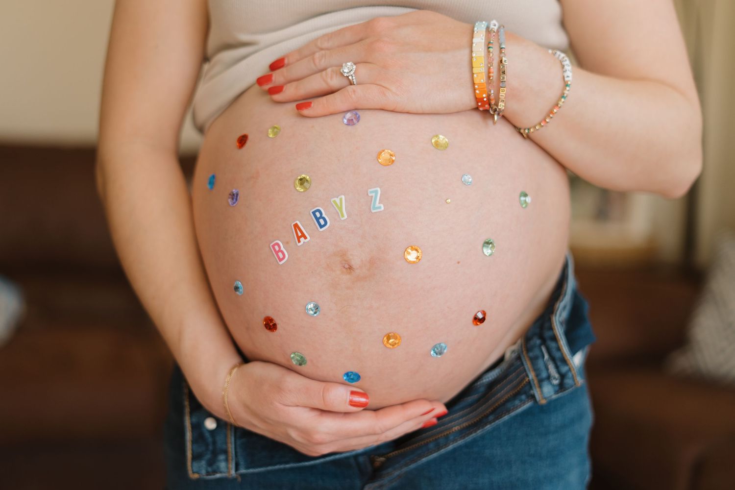 Pregnant woman's baby bump decorated with colorful gem stickers and the word BABY spelled out in letters.