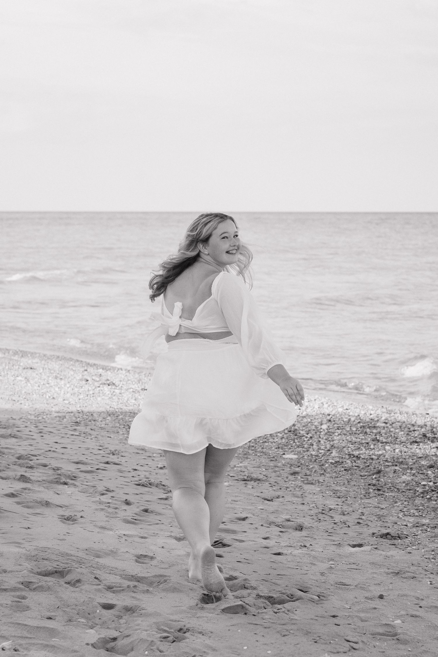 Black and white photo of blonde woman in white dress on sandy beach.