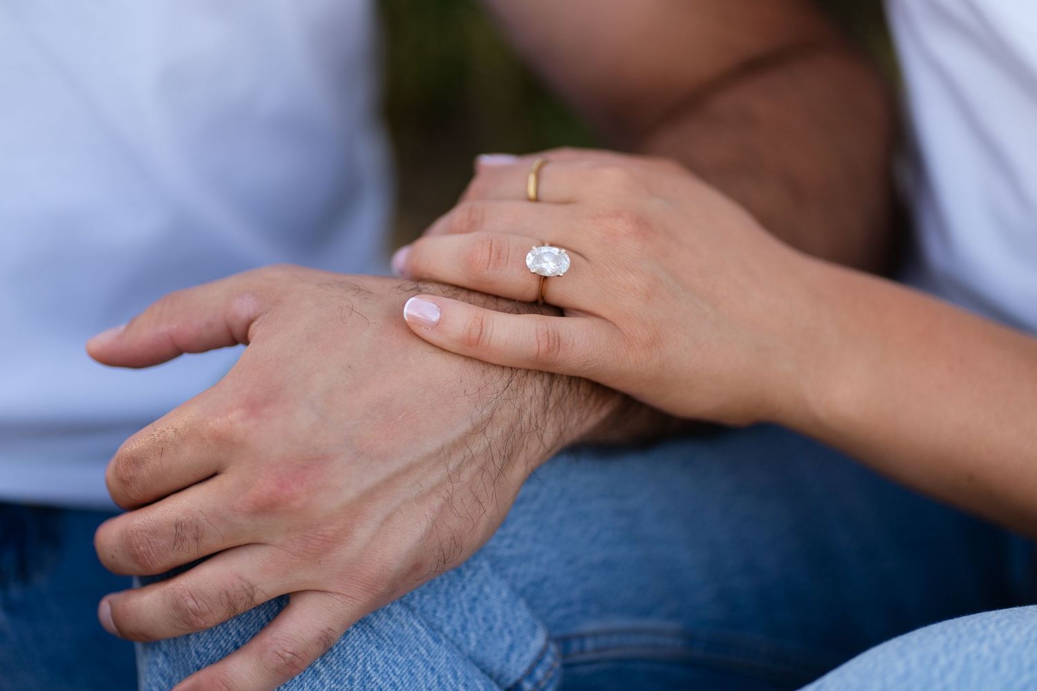 Close-up of a woman's hand wearing a large oval diamond engagement ring resting on a man's hand.