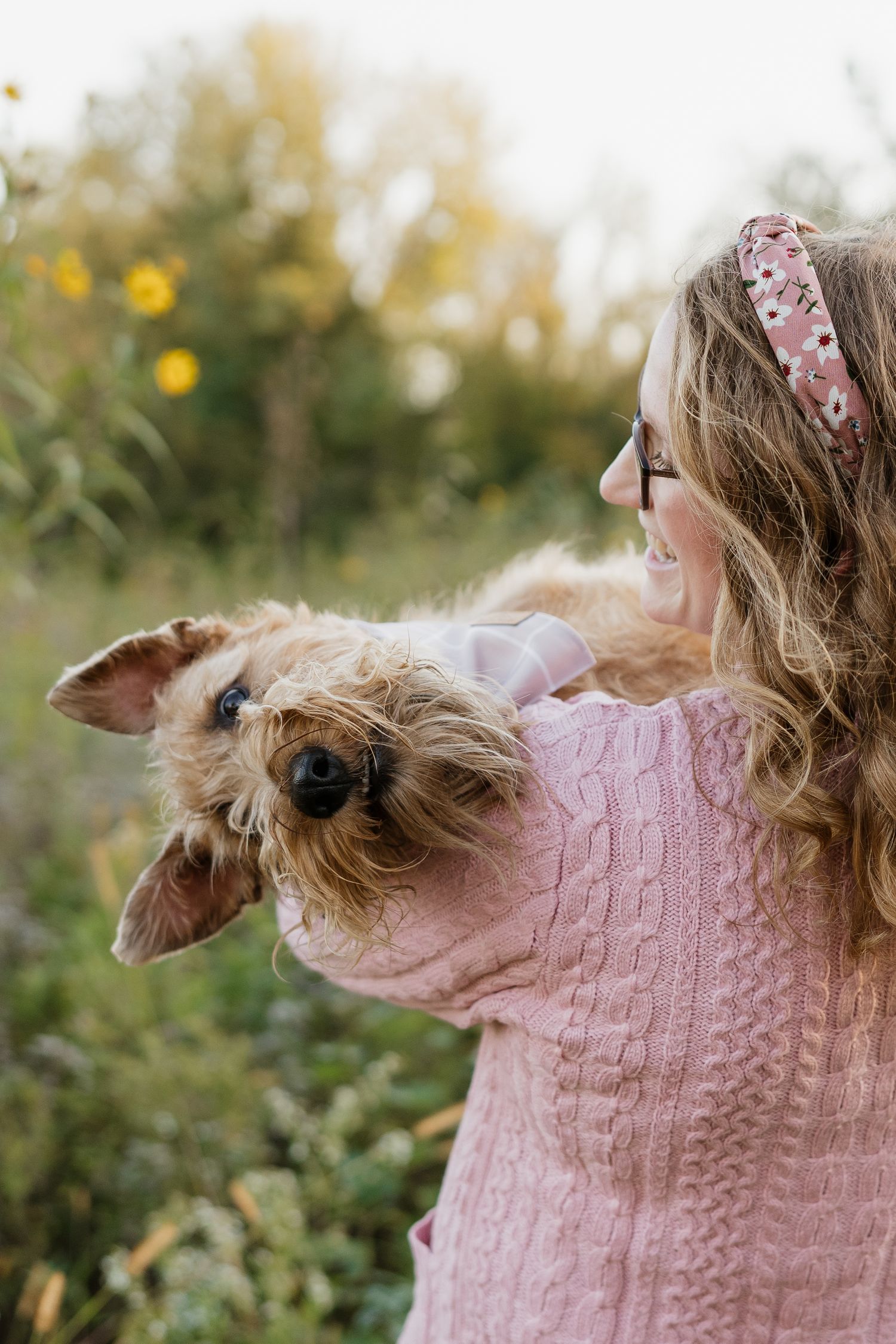 Woman in pink sweater holding a small Yorkshire Terrier dog in an outdoor autumn garden setting.