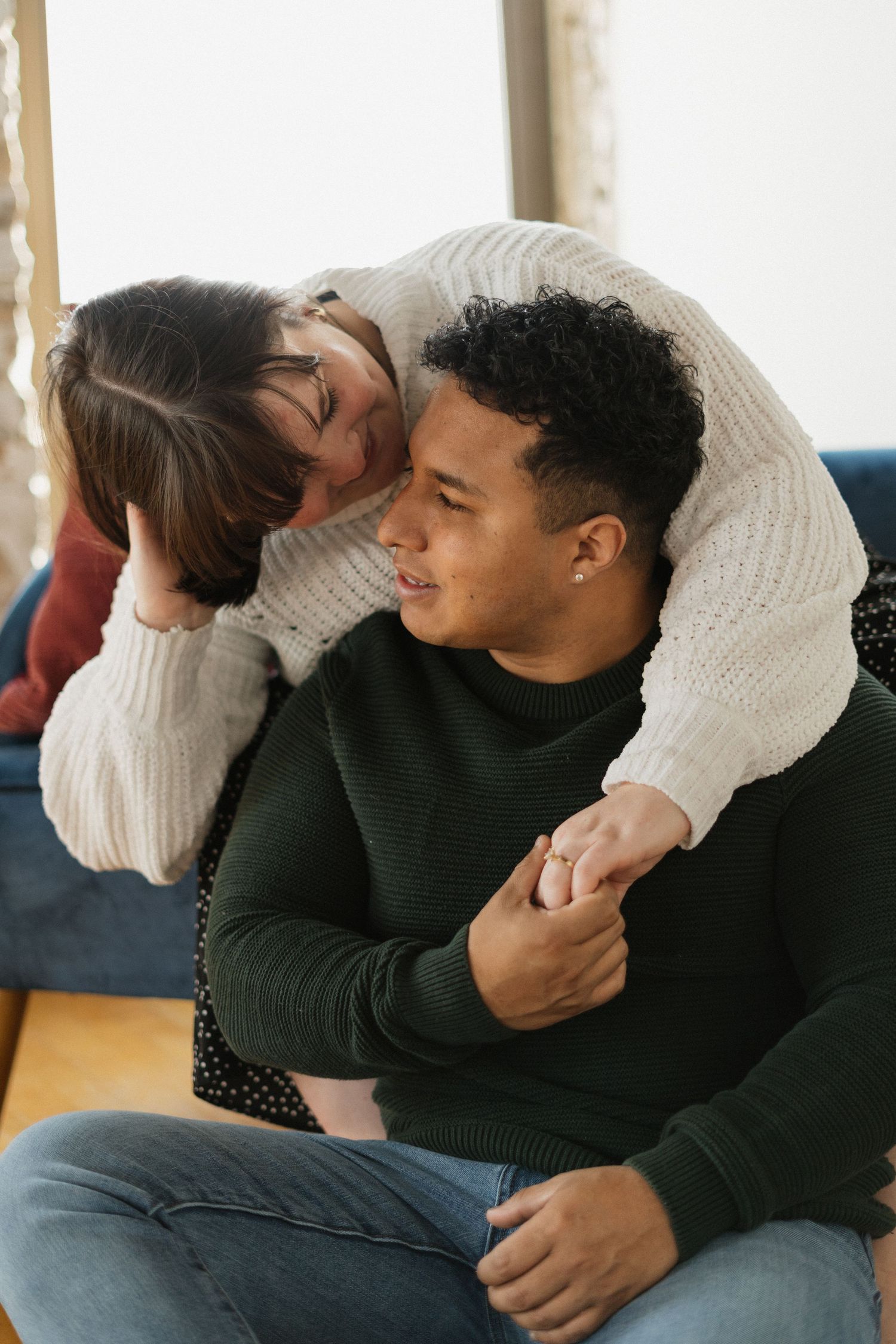 A loving interracial couple sharing a tender moment at home, woman hugging man from behind on couch.