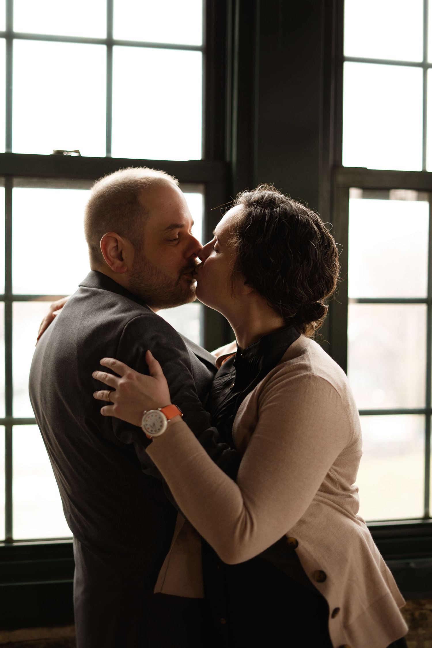 Couple sharing a romantic kiss near large industrial windows indoors.