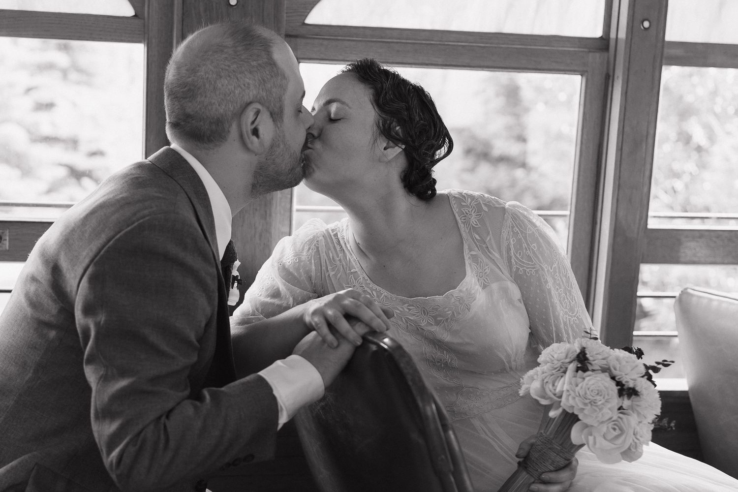 Black and white wedding photo of bride and groom sharing a kiss, bride holding bouquet.