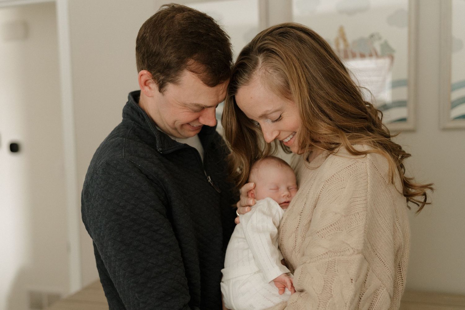 New parents smiling and gazing at their newborn baby, sharing a tender family moment indoors.