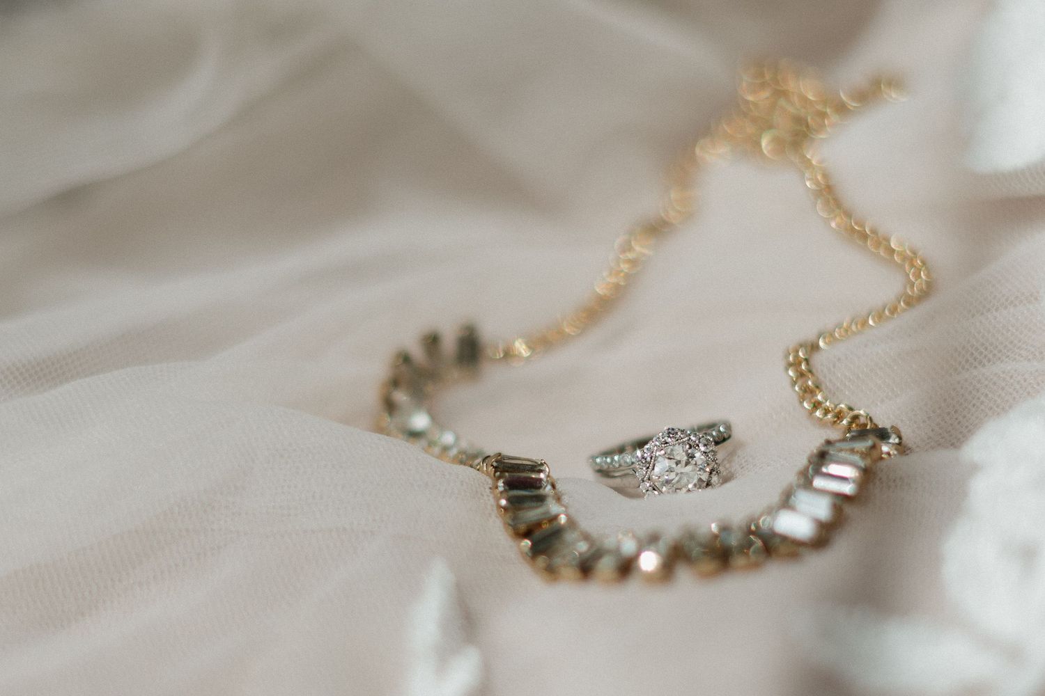 Gold chain necklace with diamond engagement ring and wedding band set displayed on white fabric.