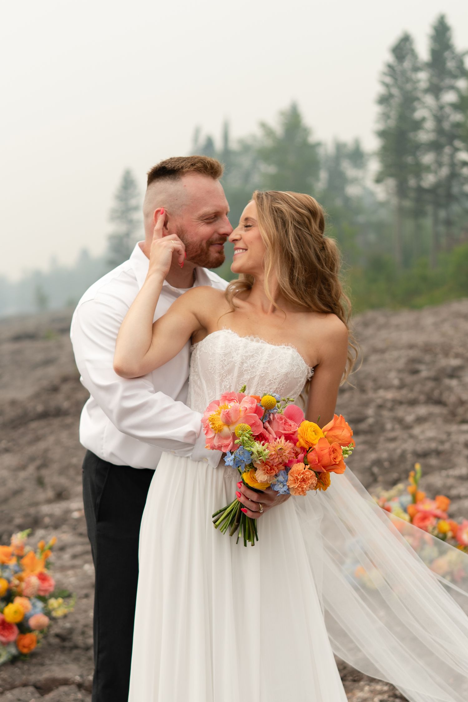 Bride and groom share a romantic moment outdoors, bride holding vibrant colorful bouquet, wearing strapless white gown.