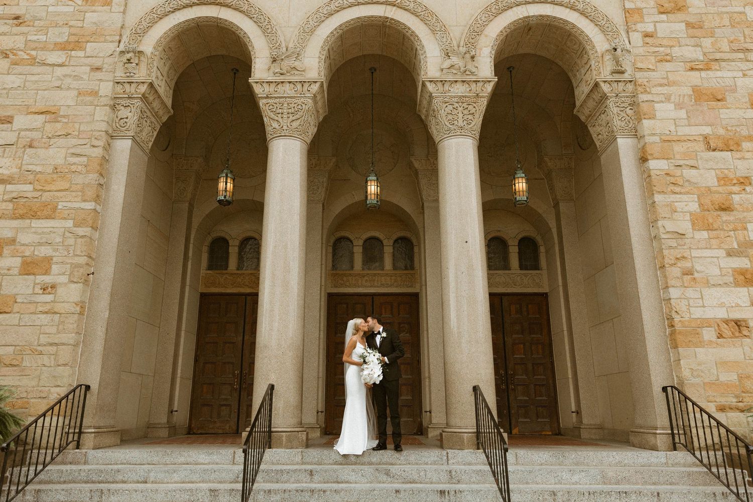 An elegant stone archway entrance to a church with wedding couple standing in the center.