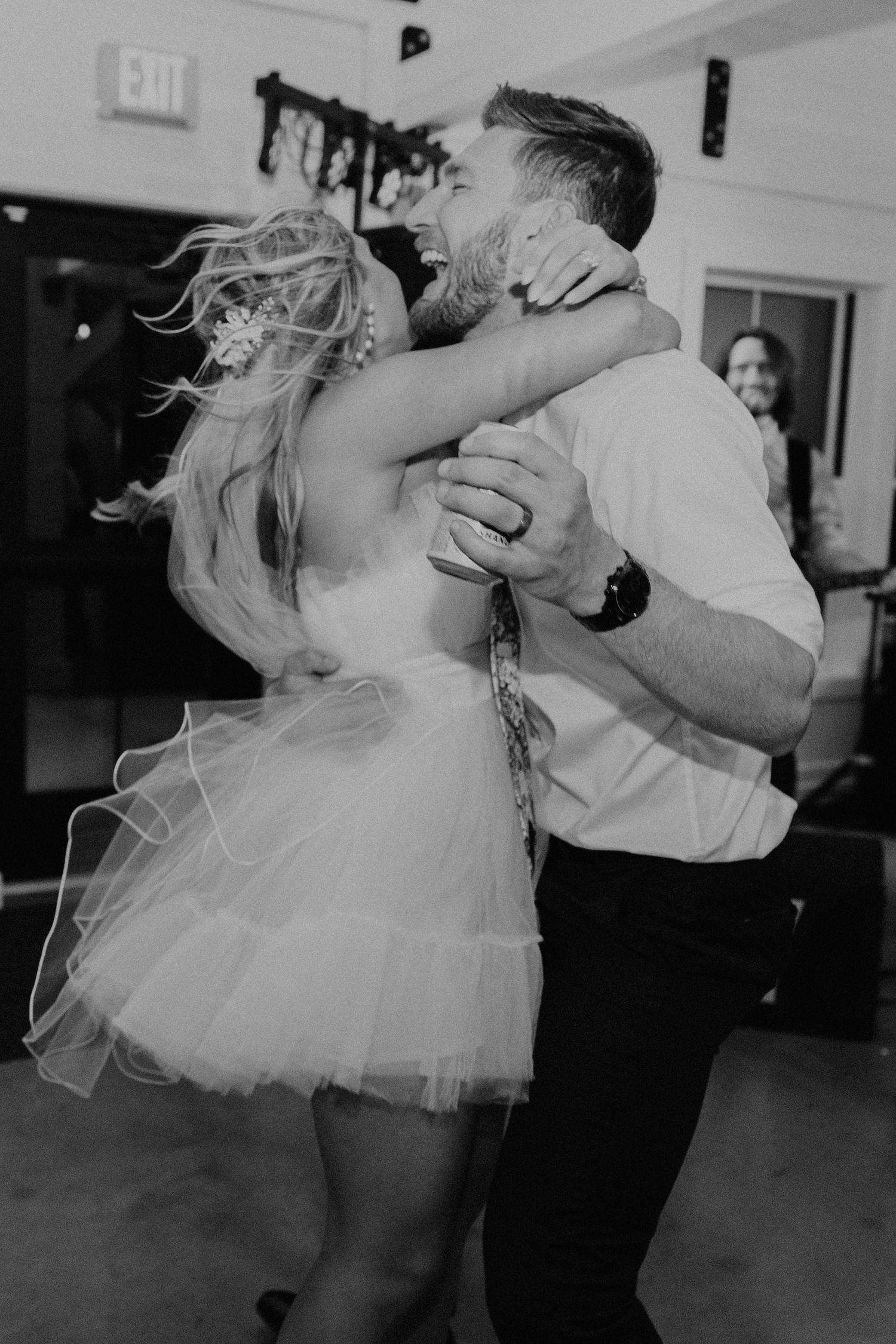 A couple dances joyfully at their wedding reception, with the bride wearing a short tulle dress.
