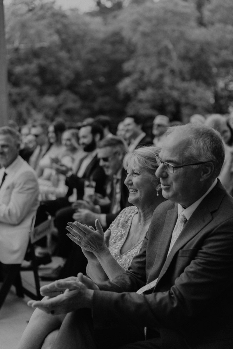 Black and white wedding guests watching ceremony with emotional expressions.