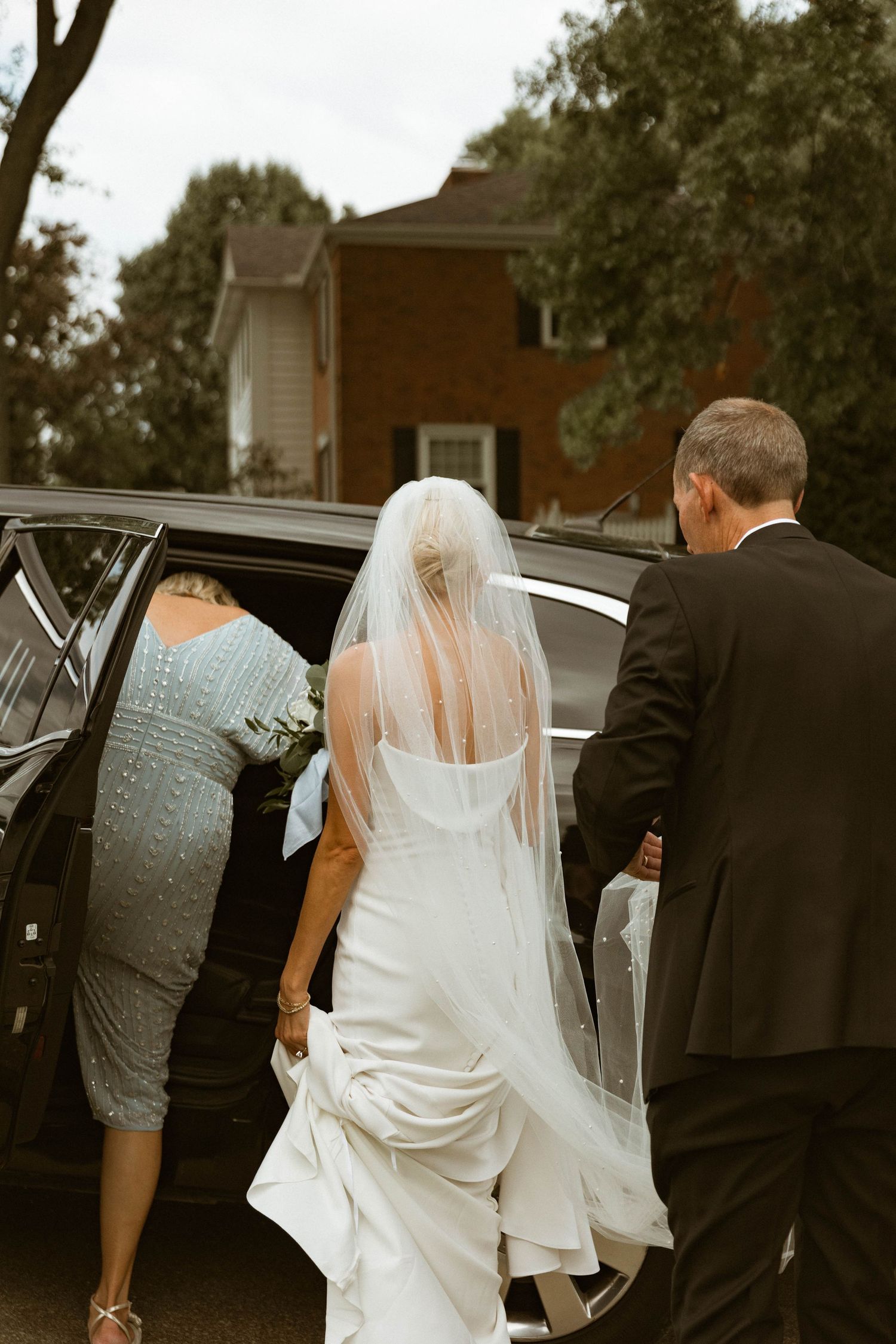 Bride in white dress getting into car with assistance on wedding day.