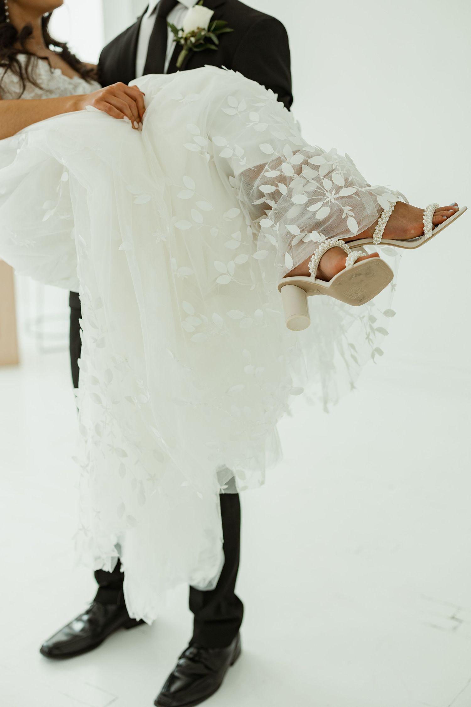 Close up details of bride and groom's formal attire showing white dress and black shoes.
