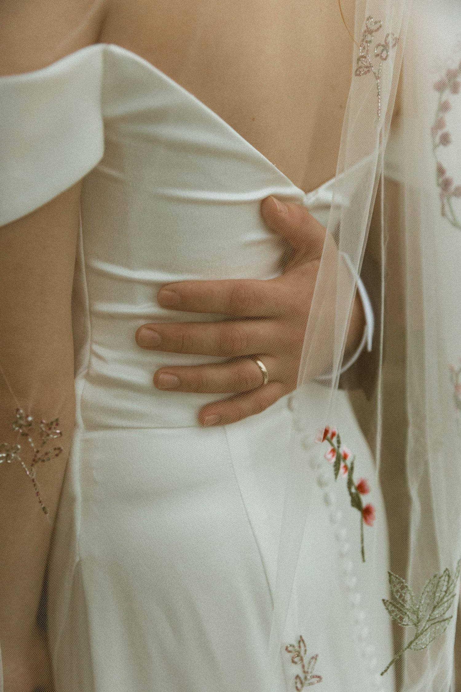Close up detail of hand with wedding ring resting on white wedding dress bodice.