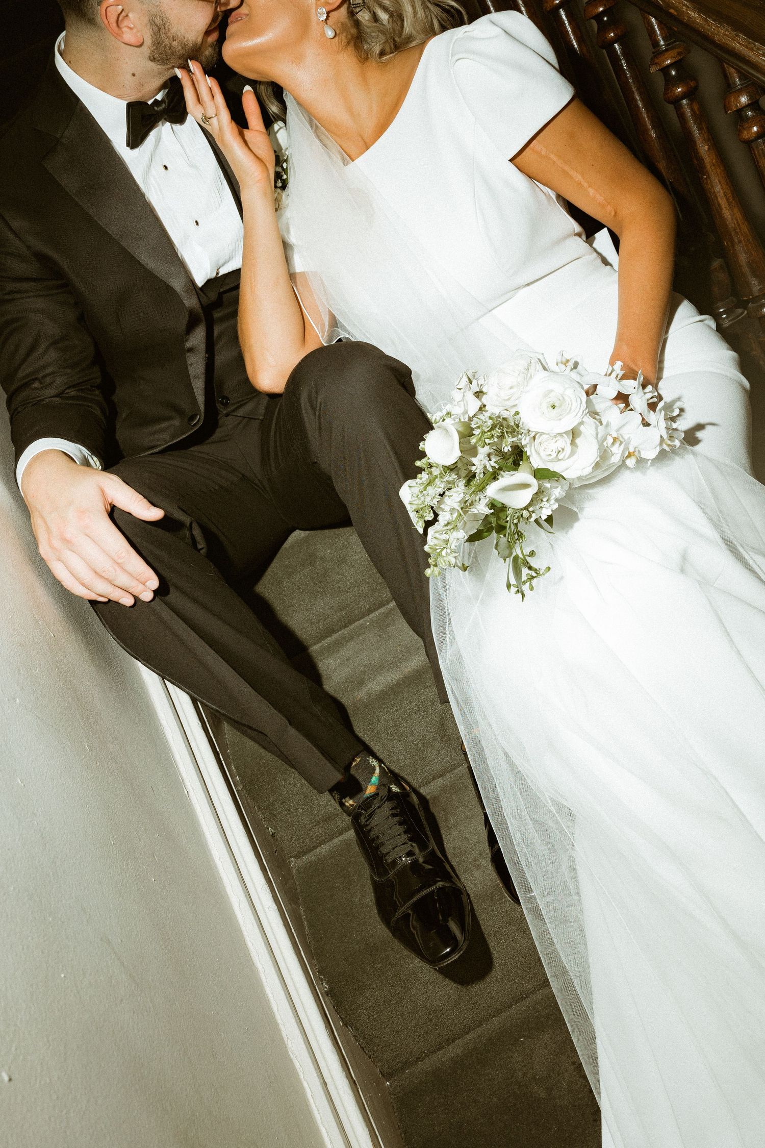 Wedding couple shares intimate moments in formal attire with white floral bouquet.