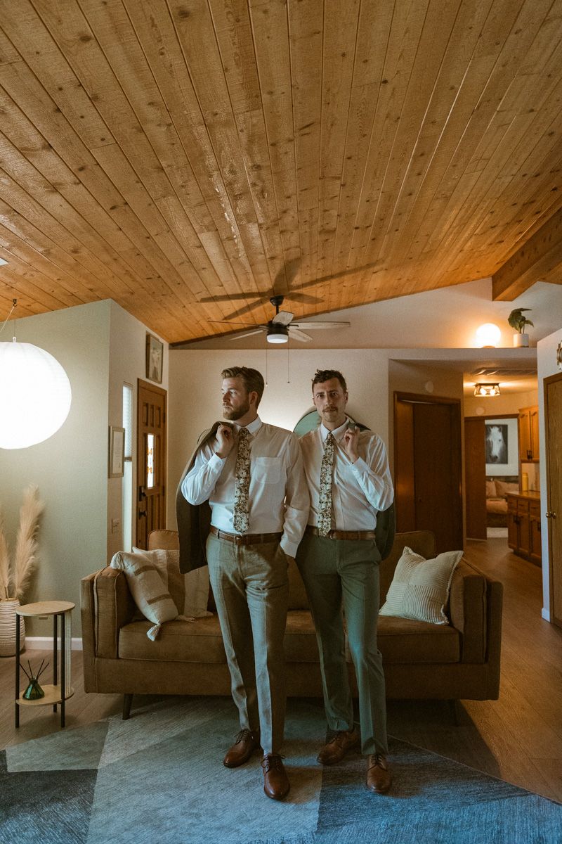 Two people adjusting their ties in a room with wooden ceiling and modern decor.