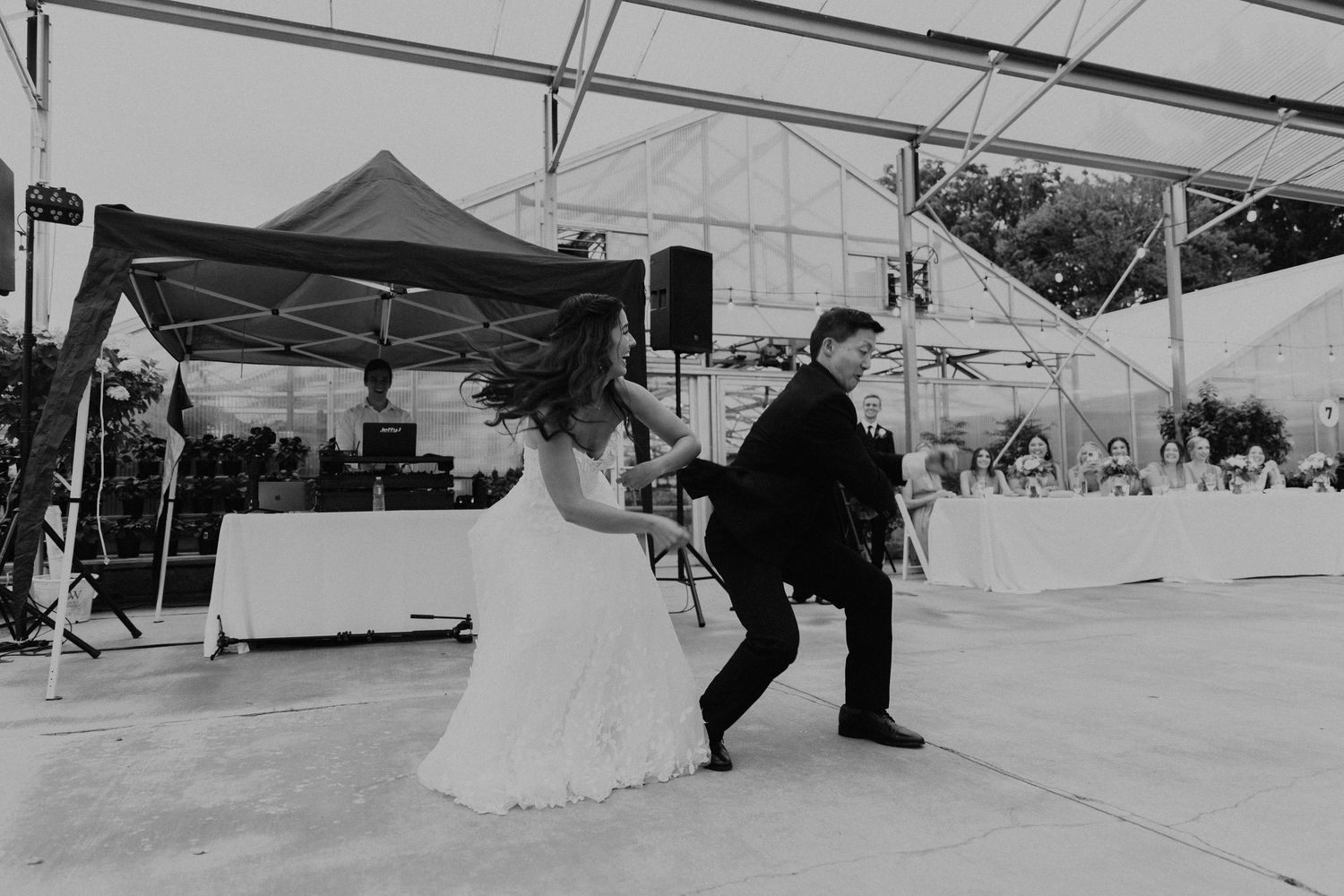 A couple dances energetically under a white tent during their reception celebration.