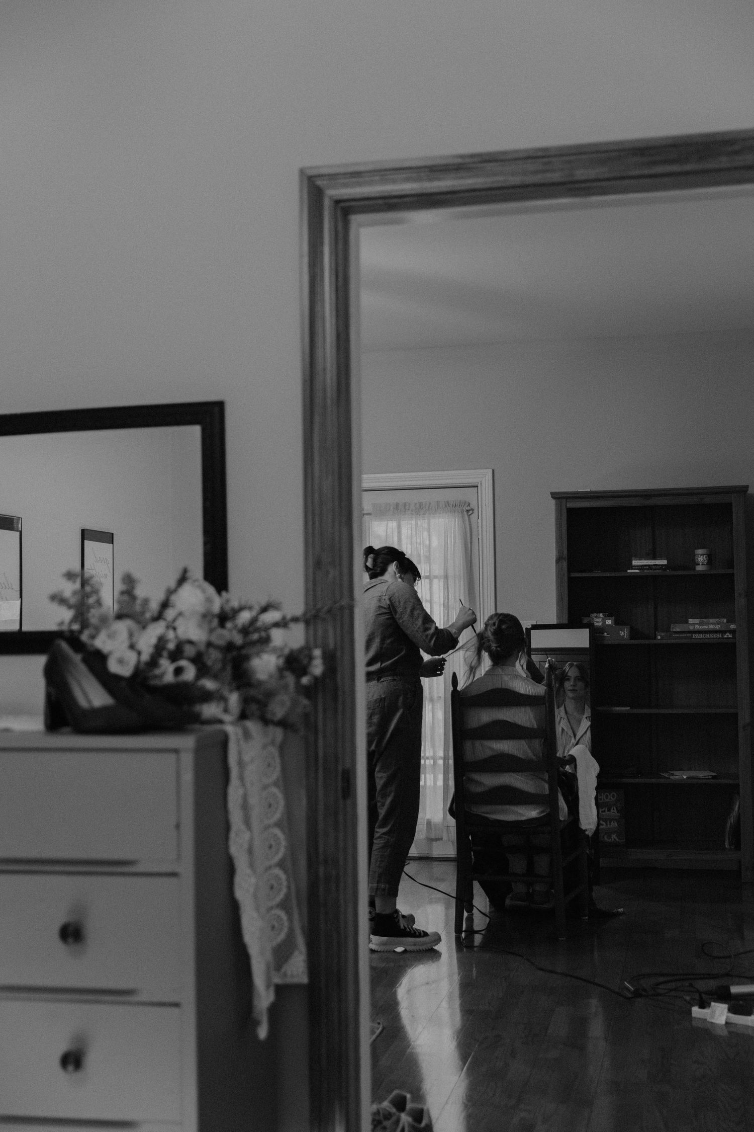 A black and white photo capturing a quiet moment through a doorway during wedding preparations.