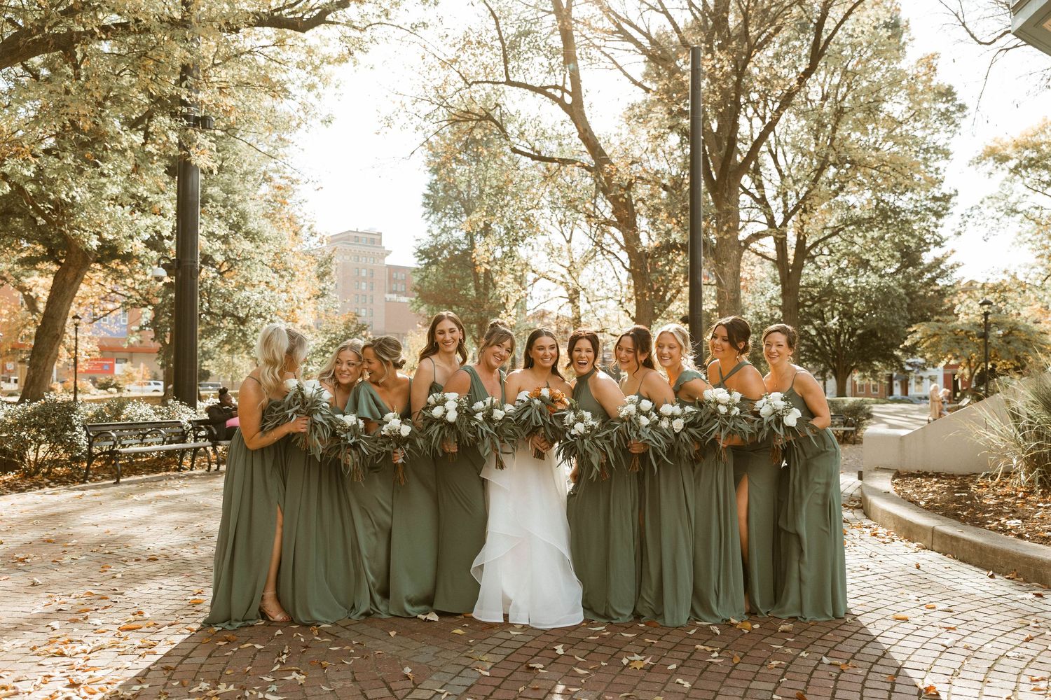 Wedding party portrait with bridesmaids wearing sage green dresses outdoors during golden hour.