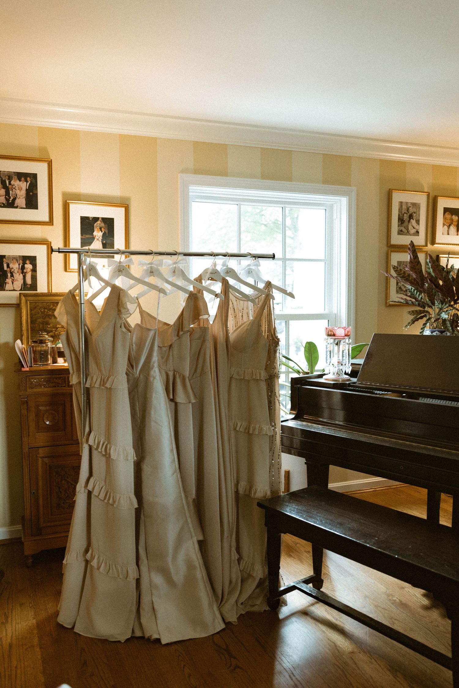 Row of matching gray bridesmaid dresses hanging neatly in a room with a grand piano.