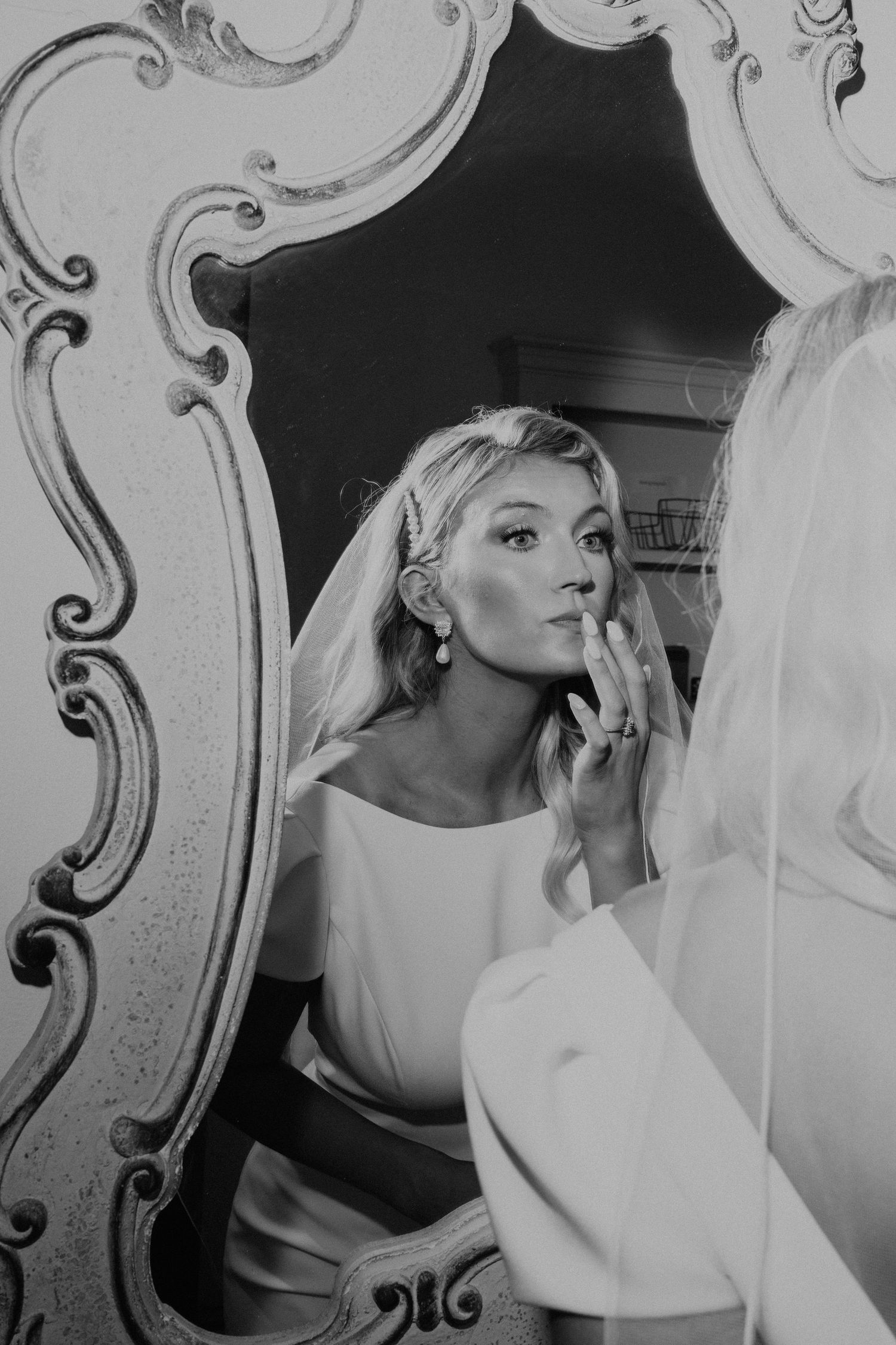Elegant black and white reflection of bride getting ready in ornate vintage mirror.