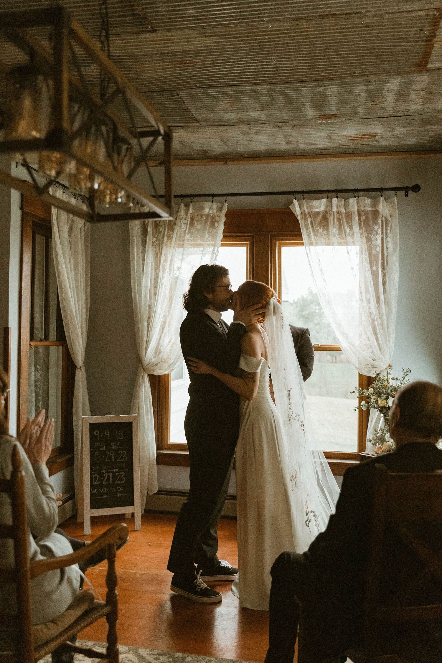A couple shares an intimate moment by lace curtains during their indoor ceremony.