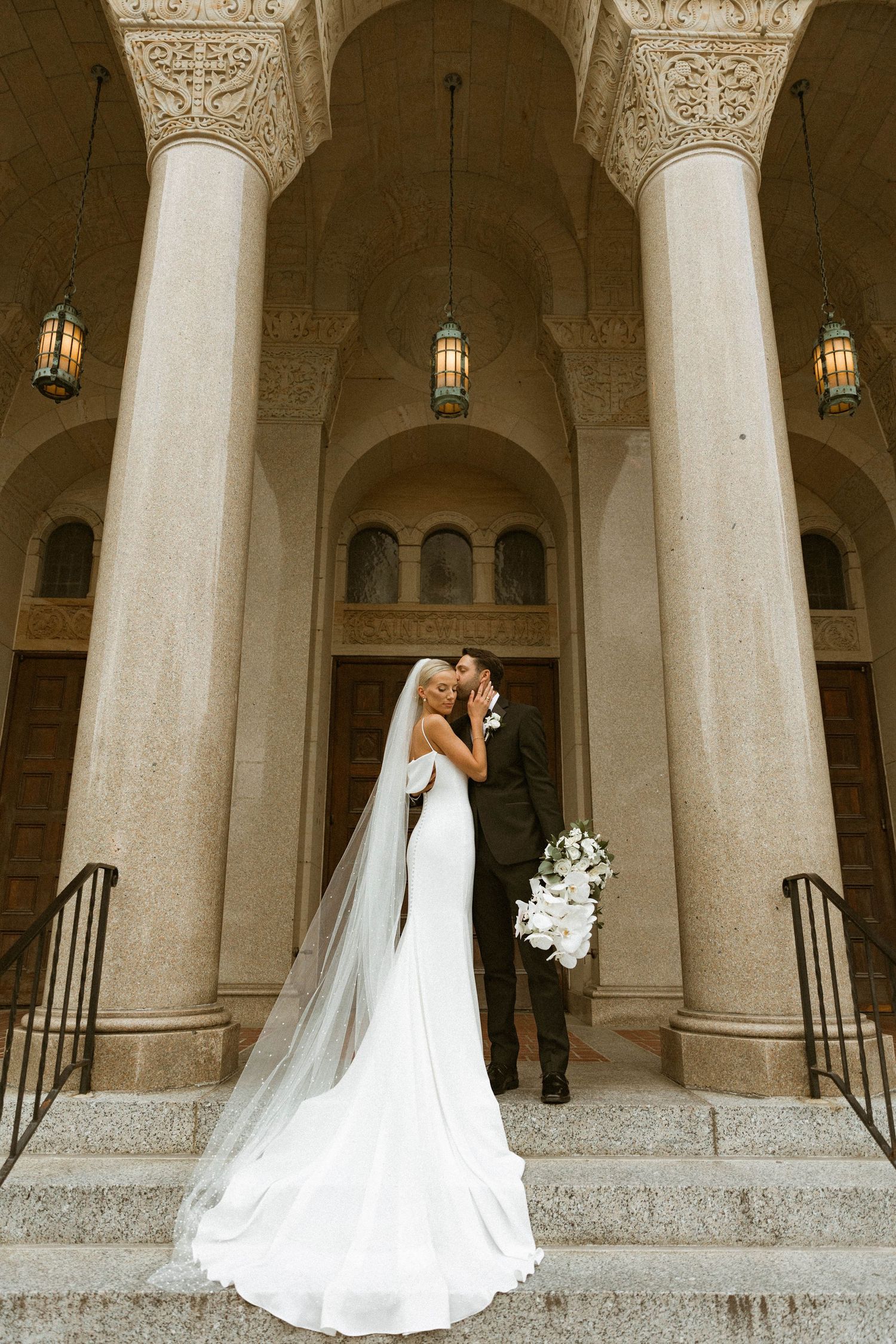 Elegant wedding couple posing under ornate stone archways and columns.