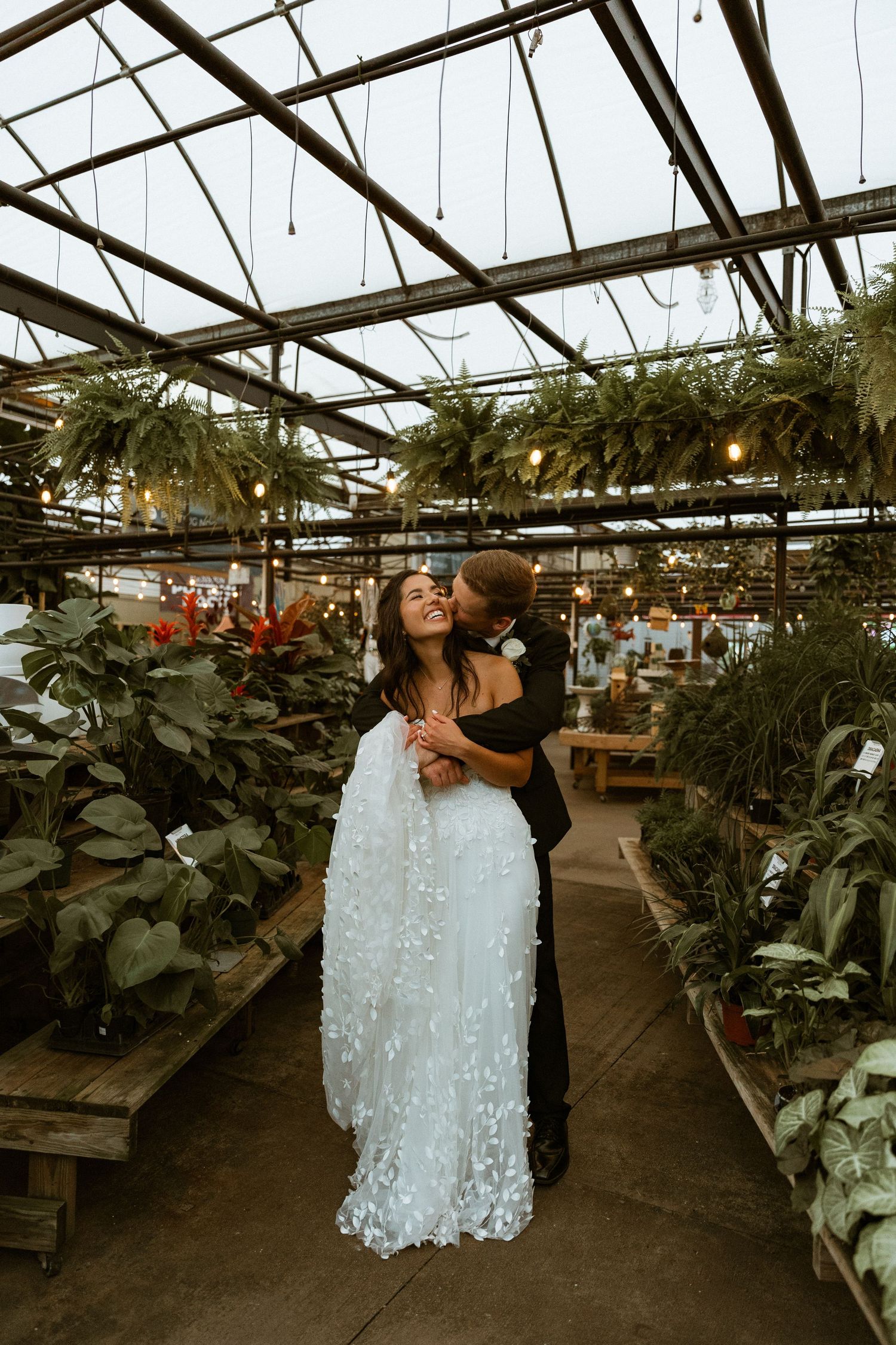Wedding couple shares romantic moments in a greenhouse filled with plants and natural light.