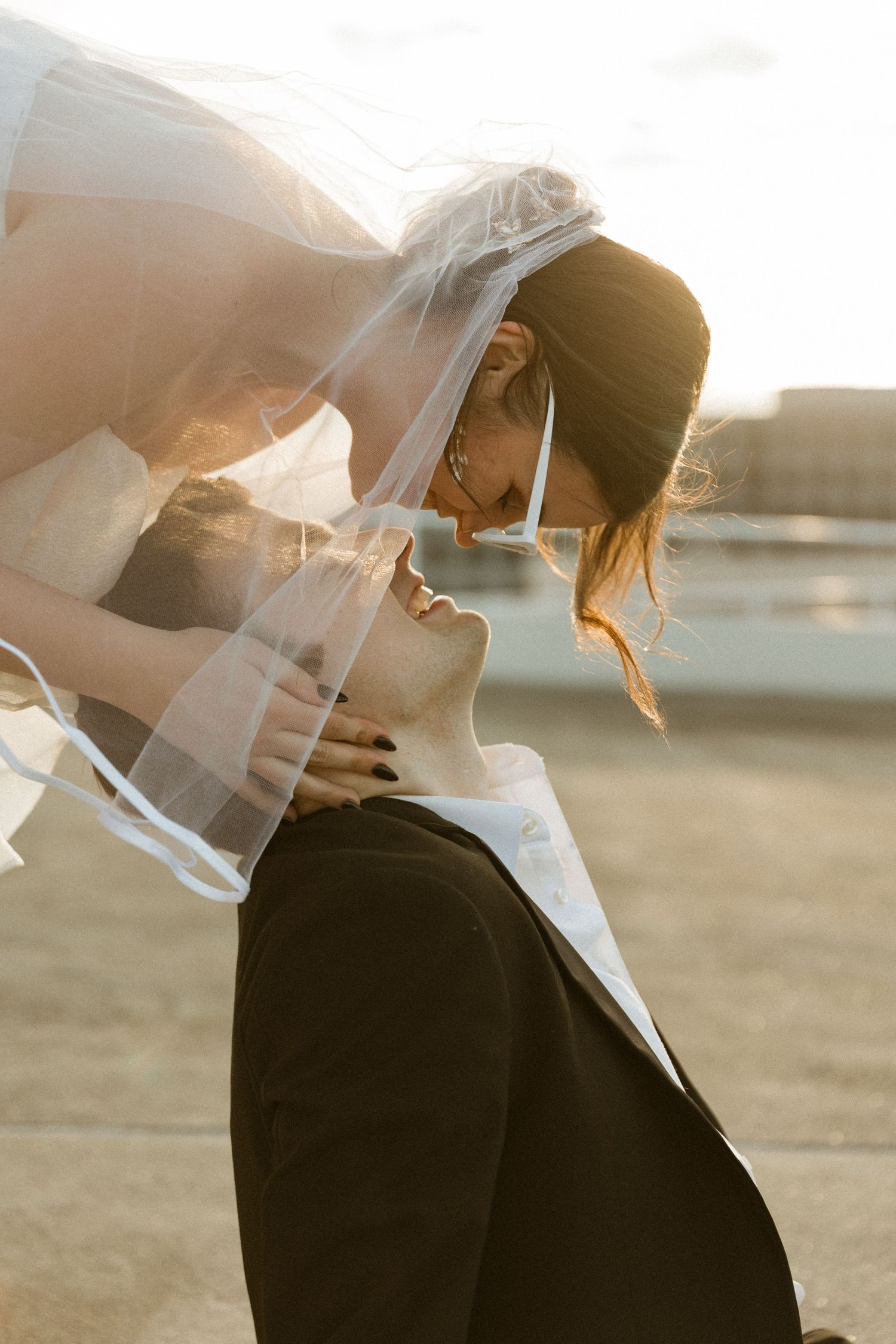Intimate sunset wedding portrait with flowing veil creating romantic silhouette.