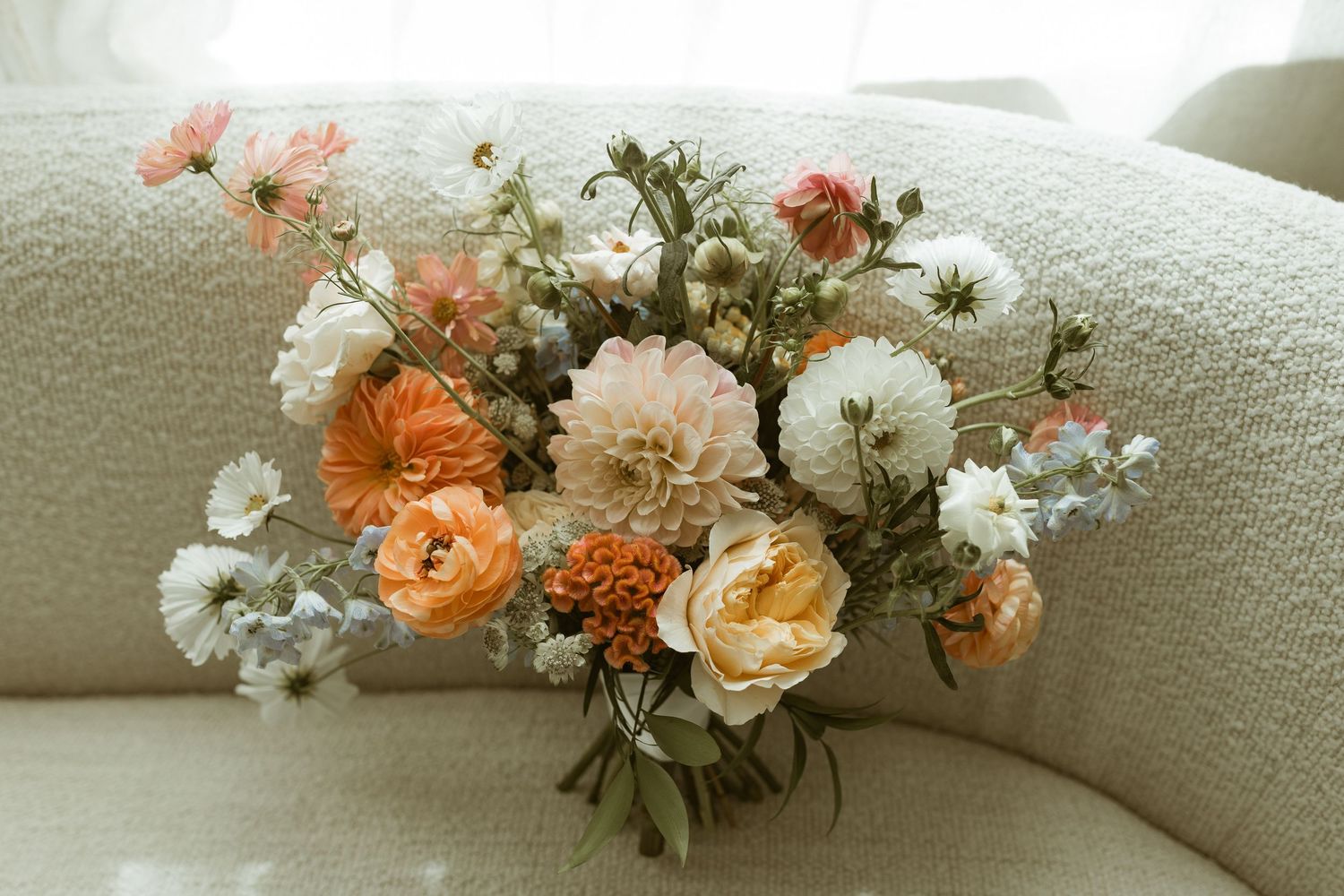 A soft pastel floral arrangement with peach and white blooms on a cream-colored couch.