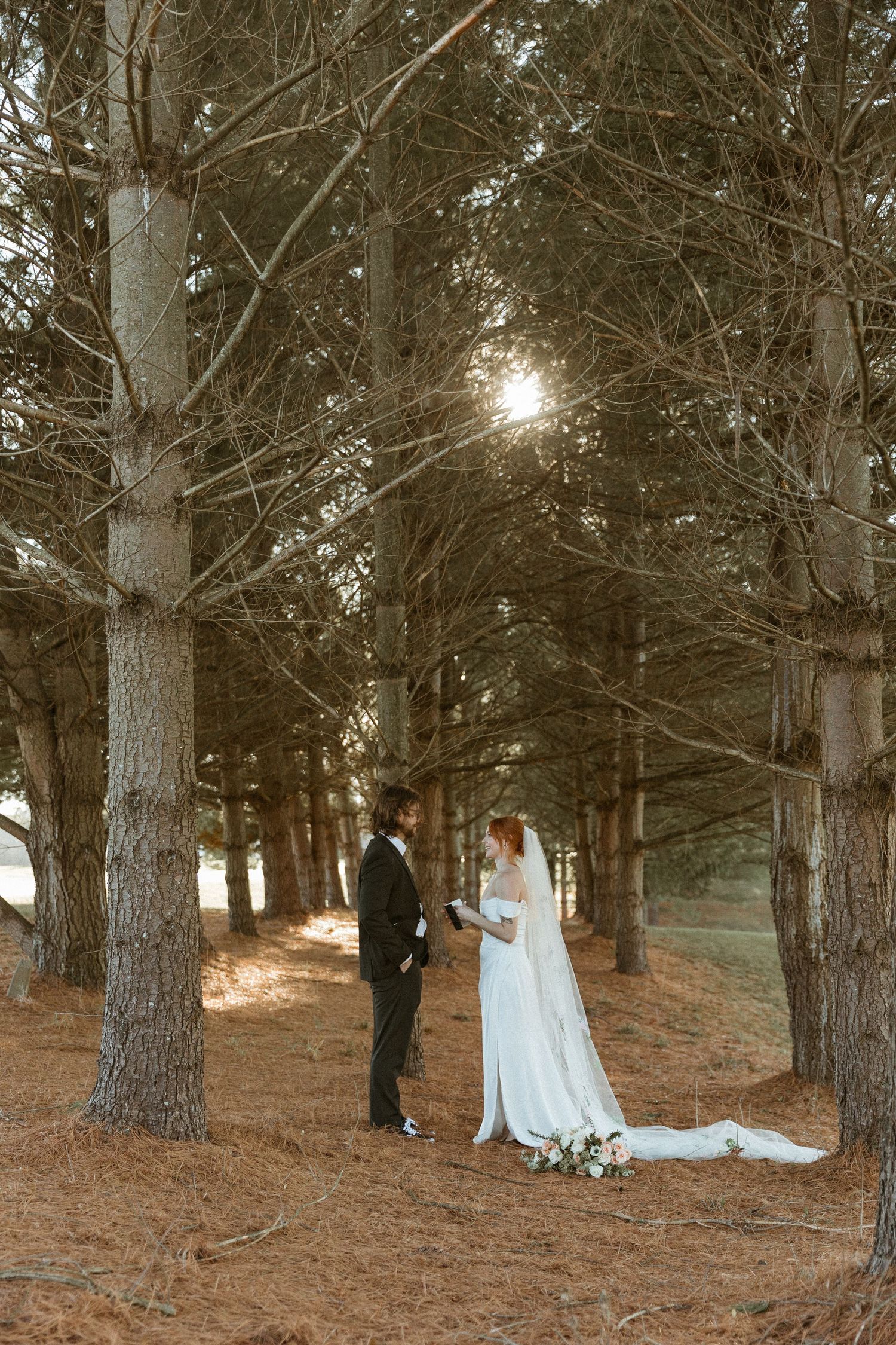 Wedding couple photographed among tall pine trees at golden hour creating romantic forest scene.