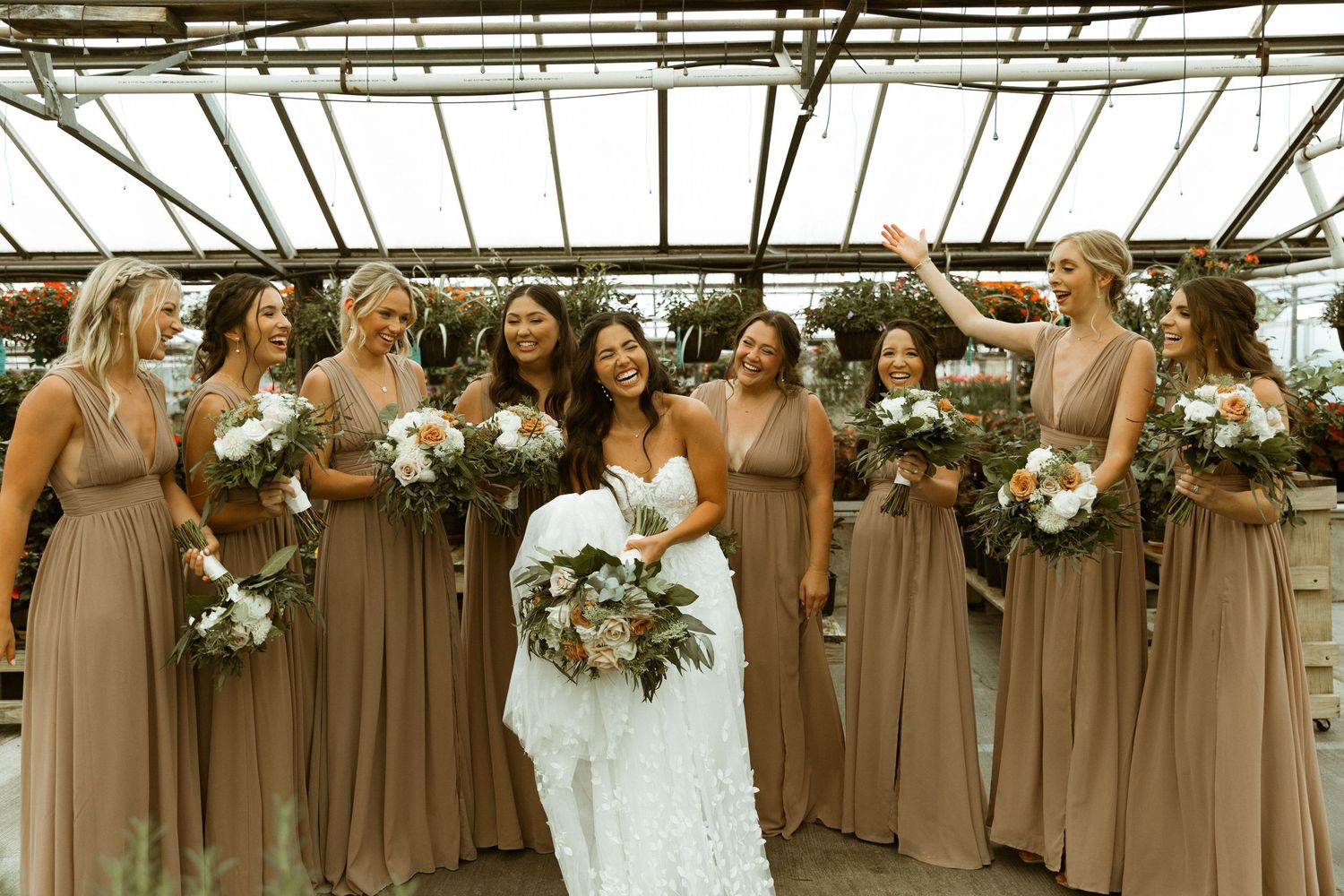 Bridal party wearing brown dresses poses together holding floral bouquets.