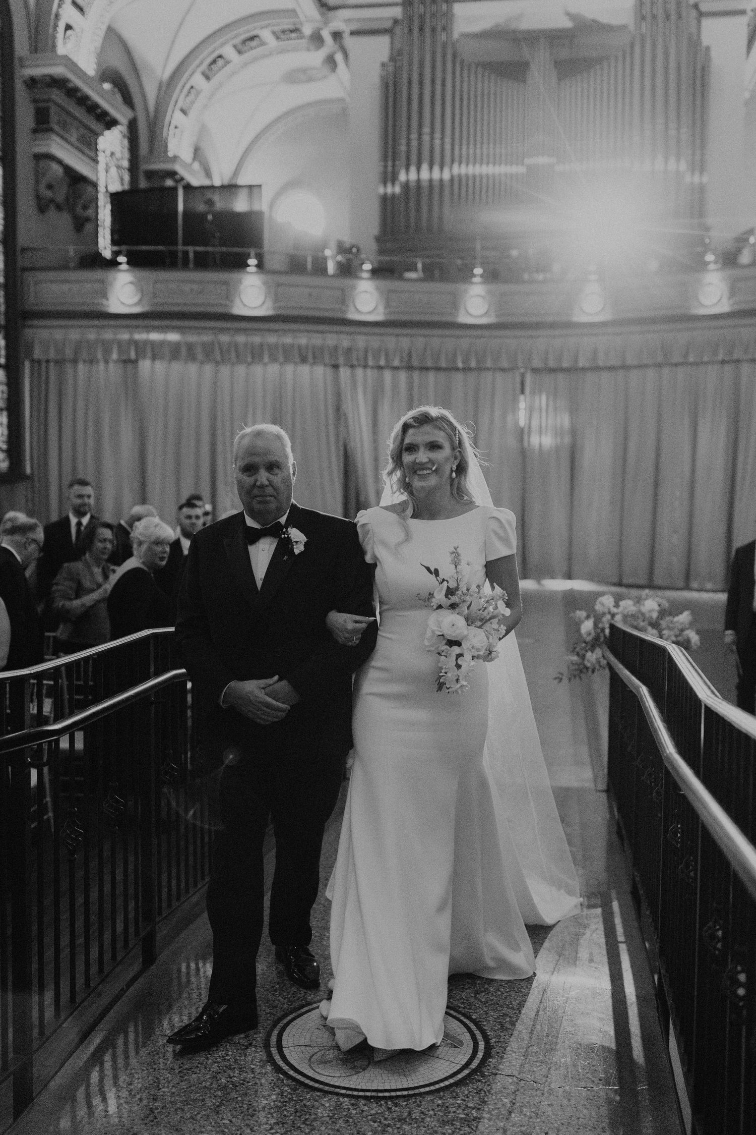 Black and white wedding ceremony photo in historic venue with dramatic lighting and architecture.