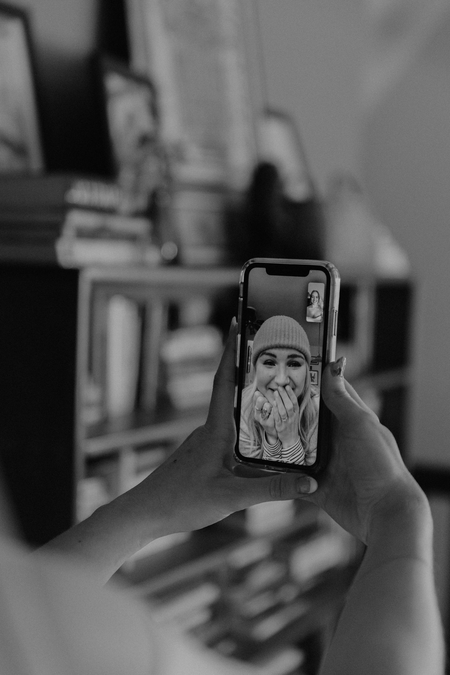 A black and white photo of hands holding a phone displaying an emotional reaction on video chat.