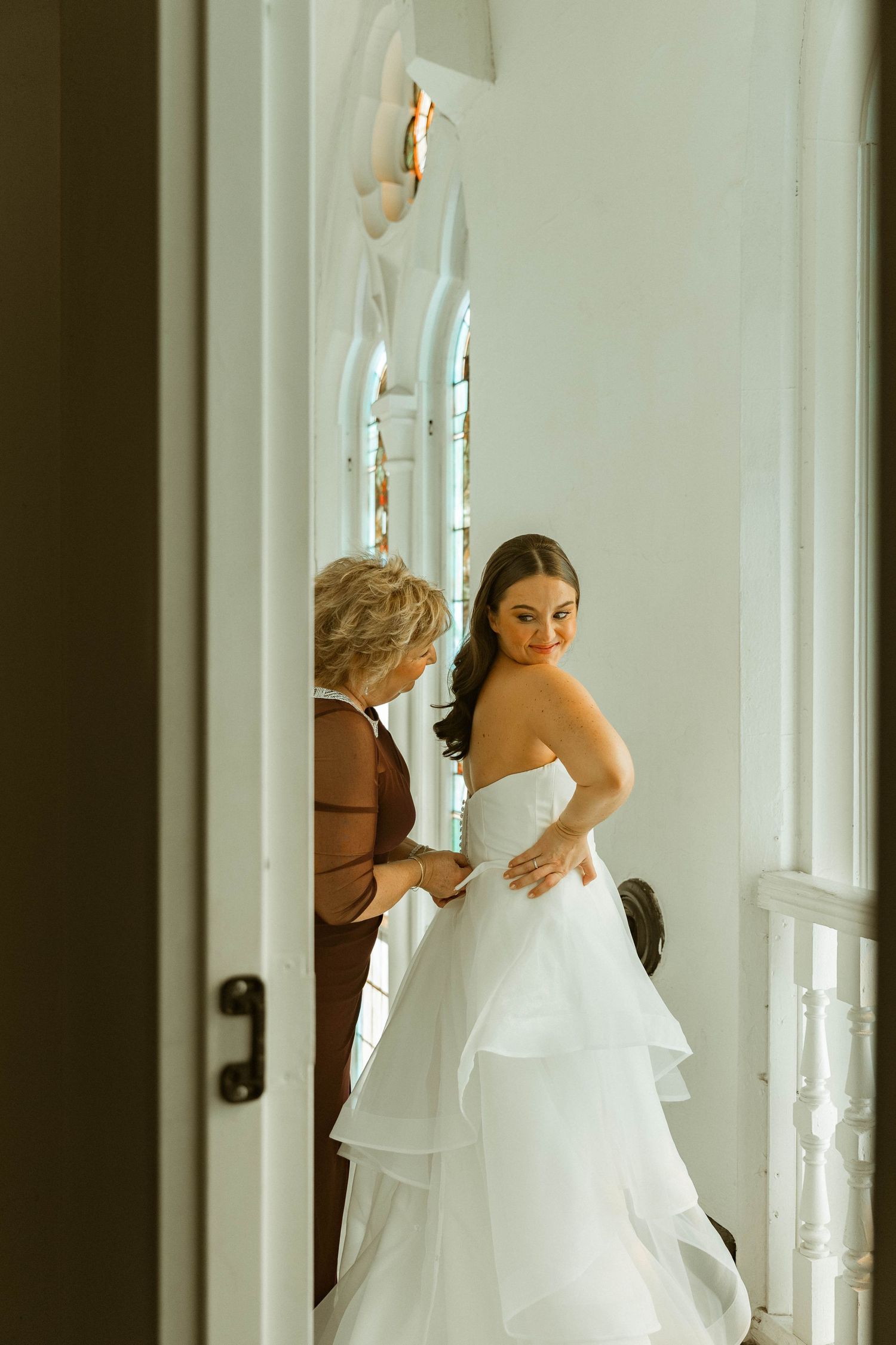 Bride getting ready in elegant white dress near window in bright room.